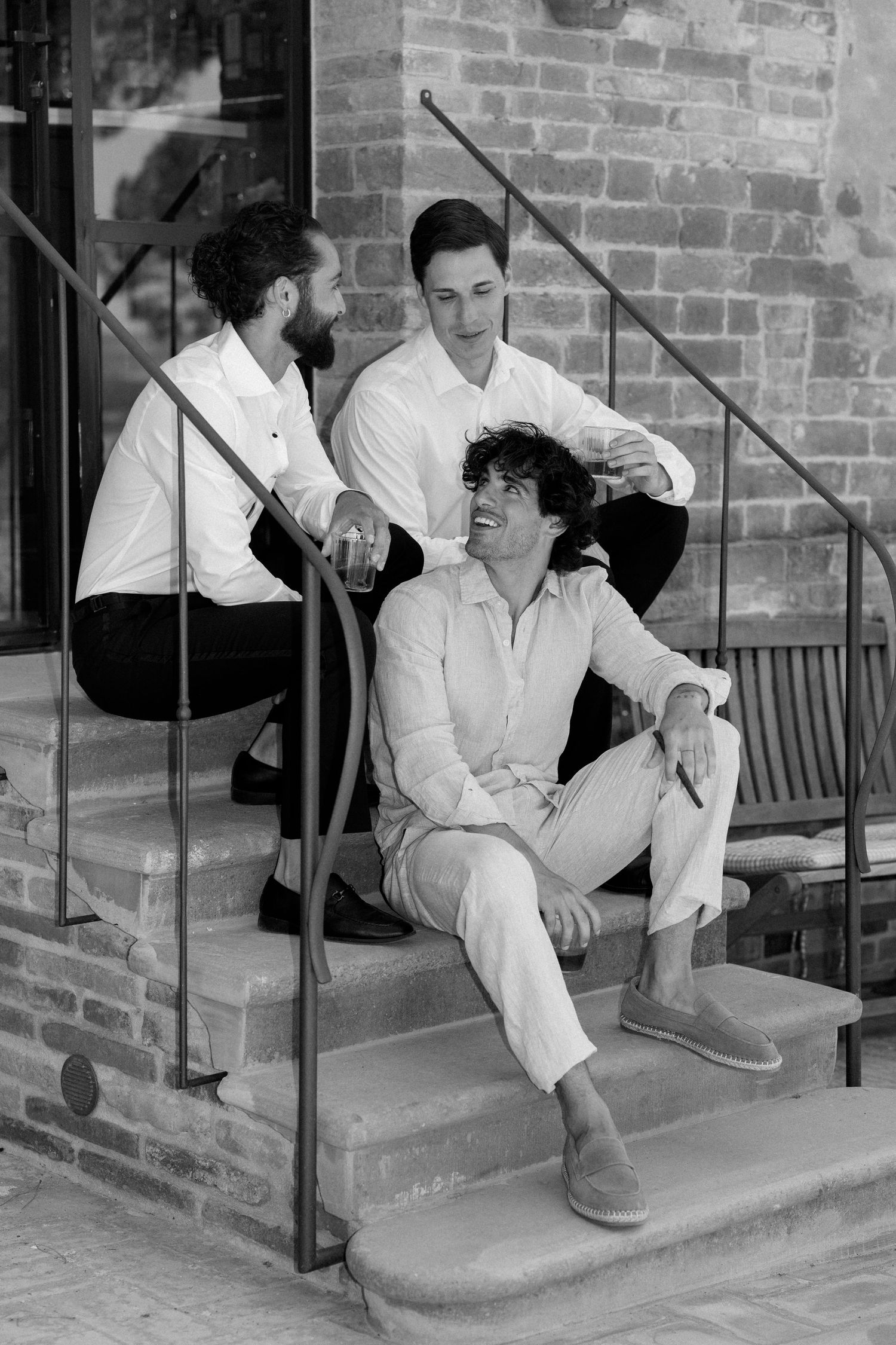 Three people relaxing on brick steps in casual white outfits in black and white photograph.