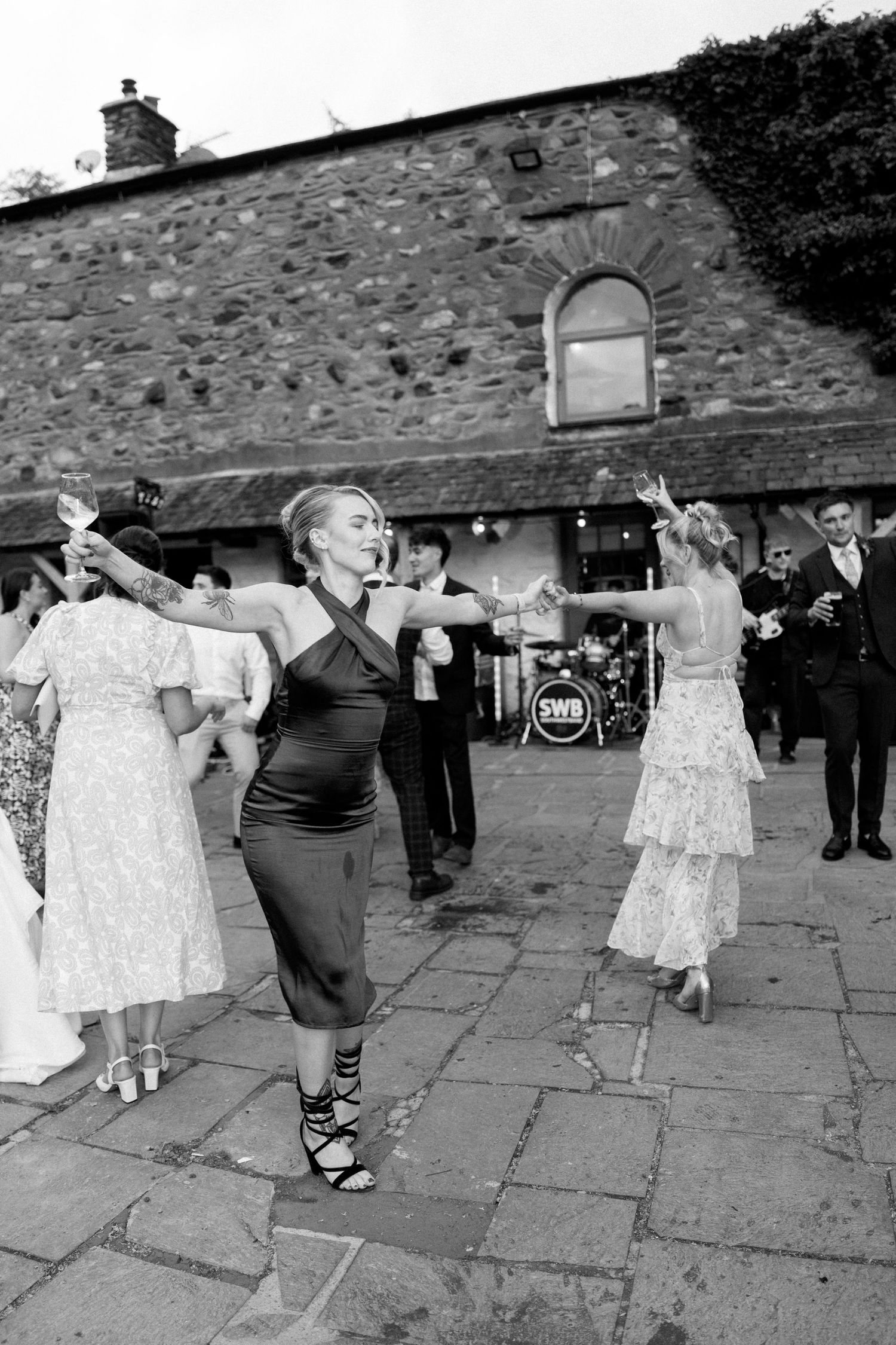Wedding celebration with guests dancing on stone patio outside rustic building.