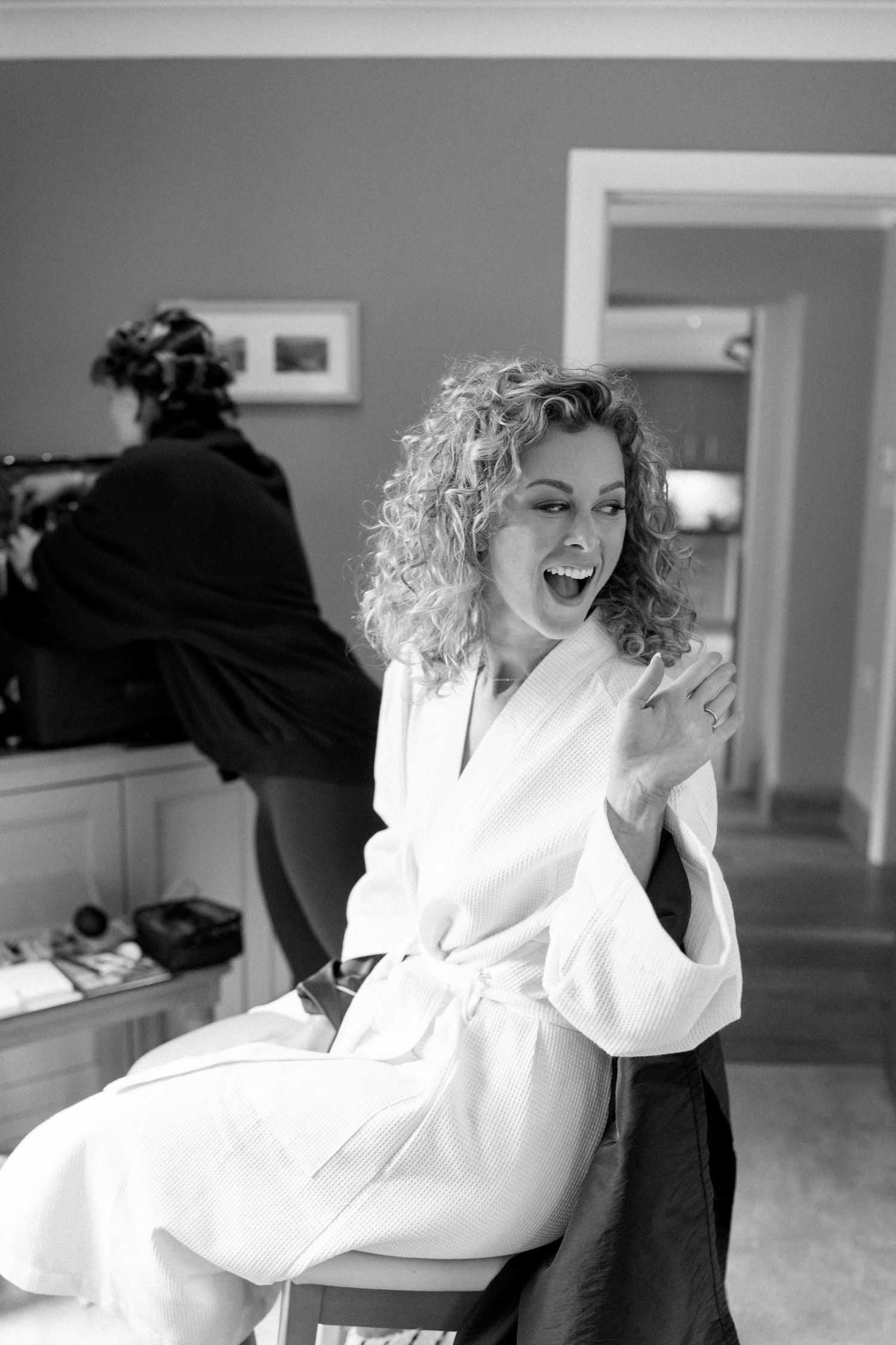 Black and white portrait of someone in a white bathrobe laughing joyfully while getting ready.