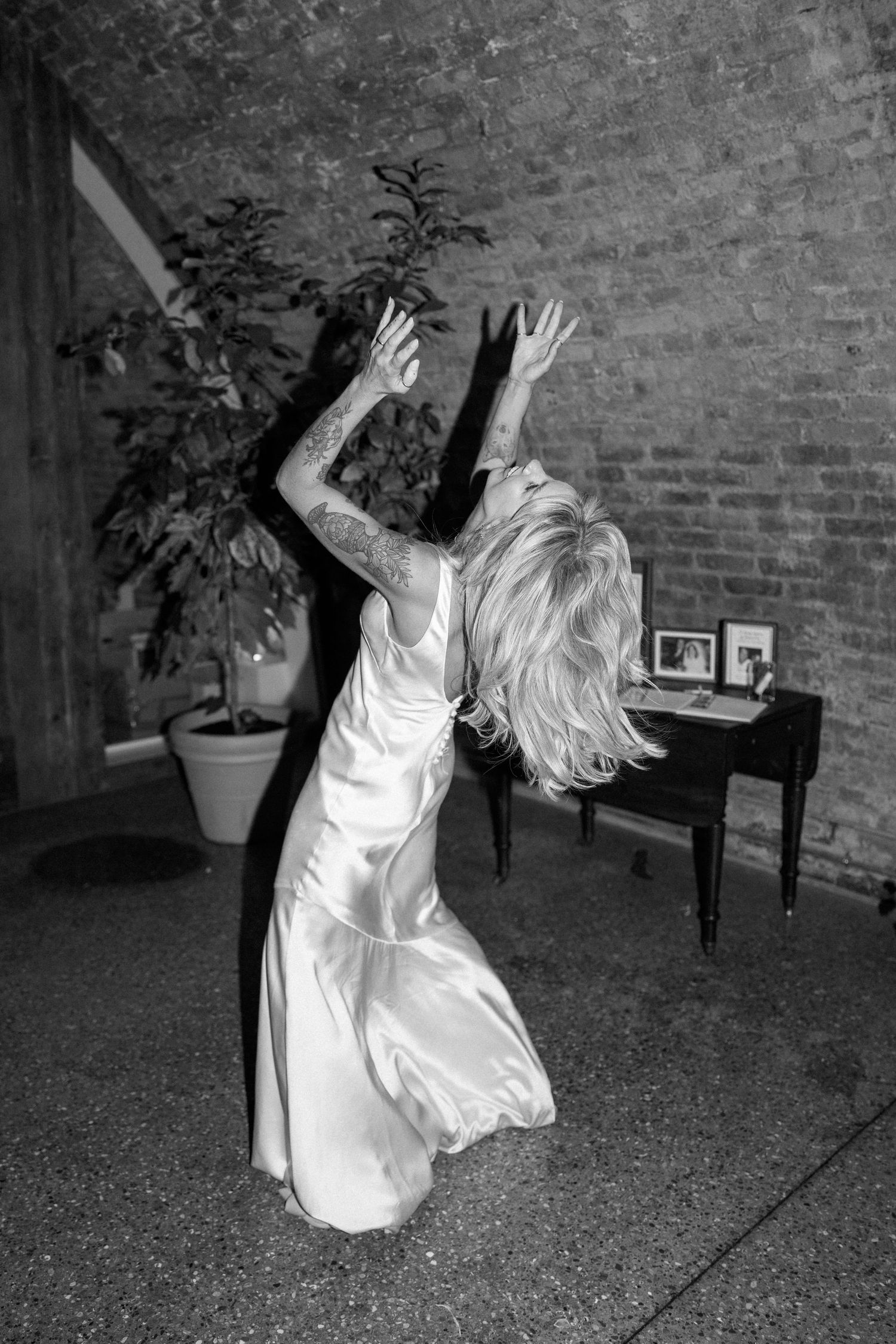 Black and white sequence showing a person in white dress dancing expressively against a brick wall.