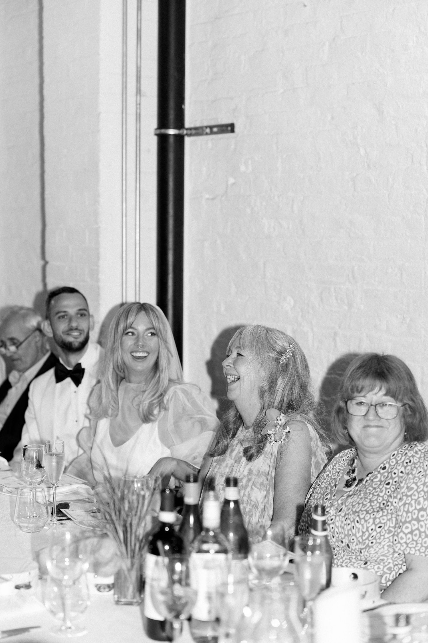 Wedding reception dinner with guests seated at a long table with white decor and wine glasses.