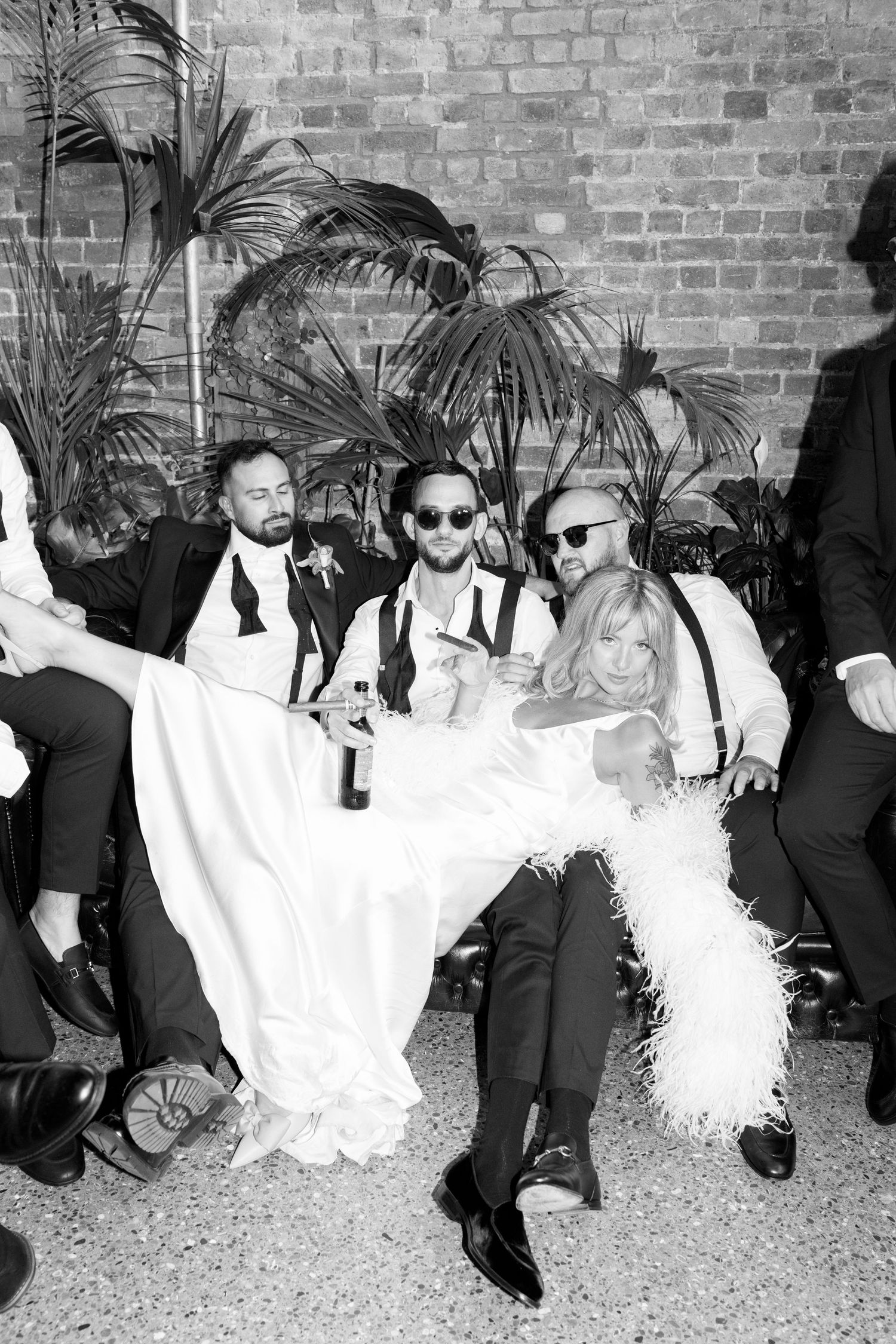 Wedding party in formal attire striking fun poses against brick wall background.