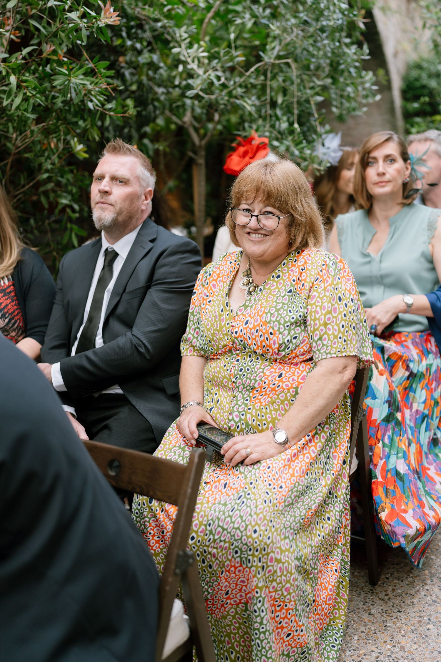 Wedding guests seated outdoors in formal attire during a garden ceremony.