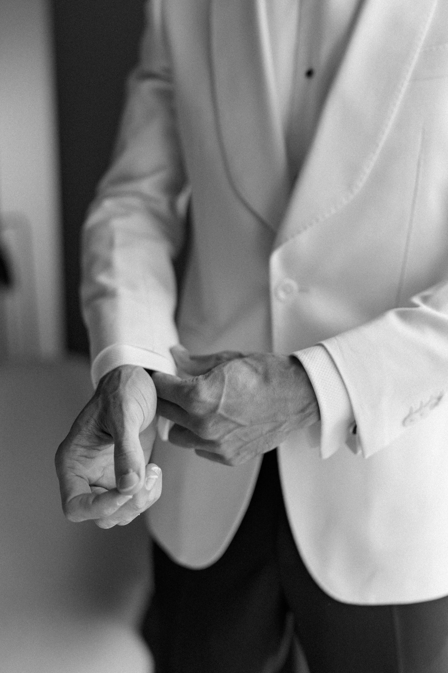 Close-up of hands adjusting cufflinks on a white tuxedo jacket sleeve.