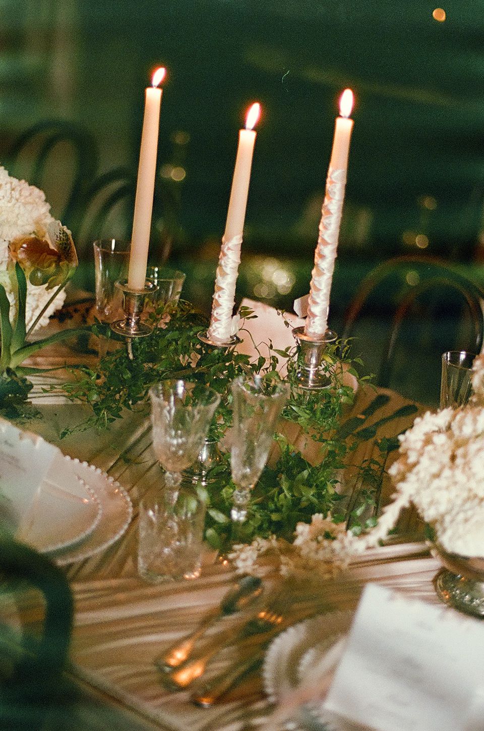 Elegant table setting with lit white taper candles and delicate greenery garland creating a romantic ambiance.