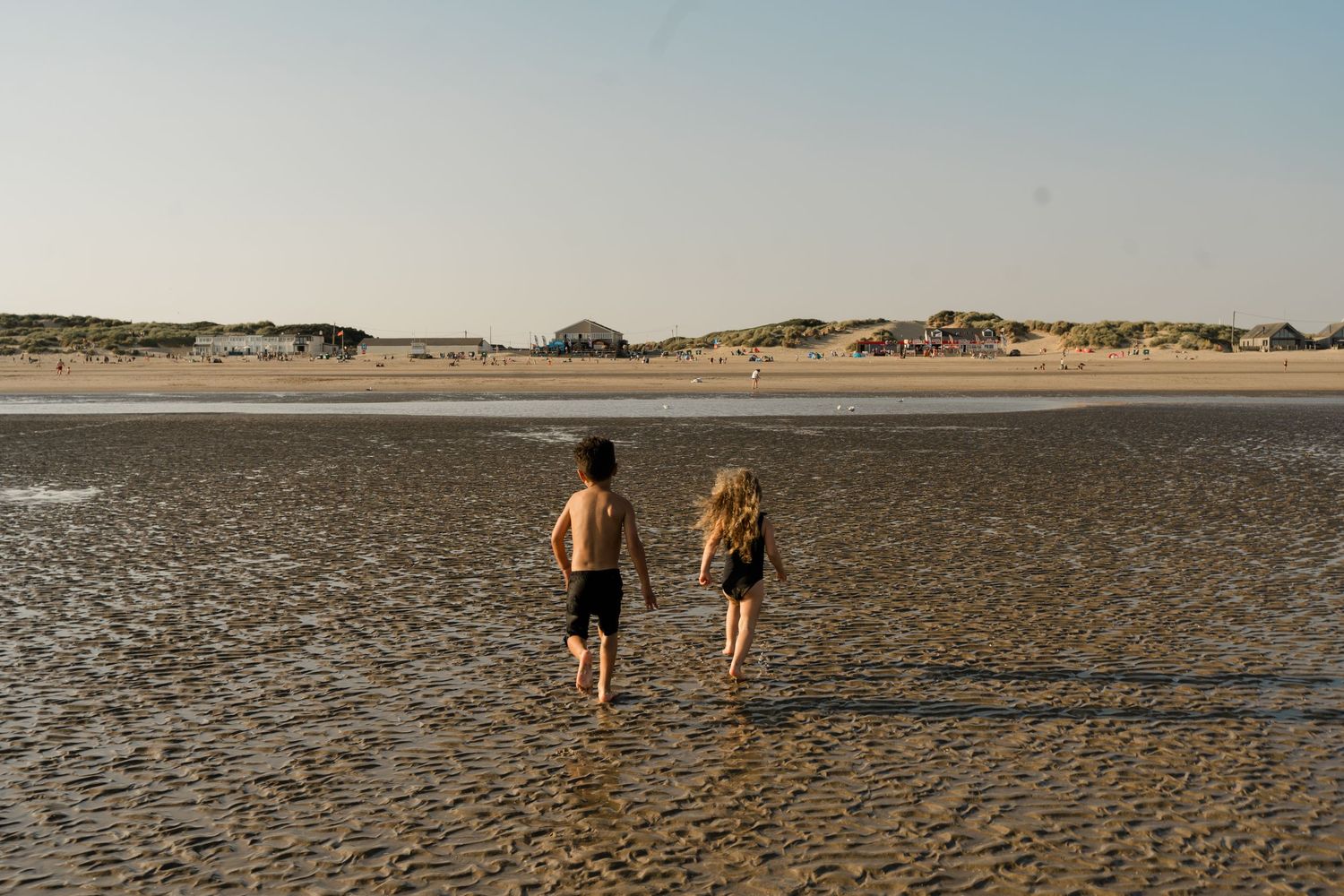 Wide view of two people walking on a vast empty beach at sunset.