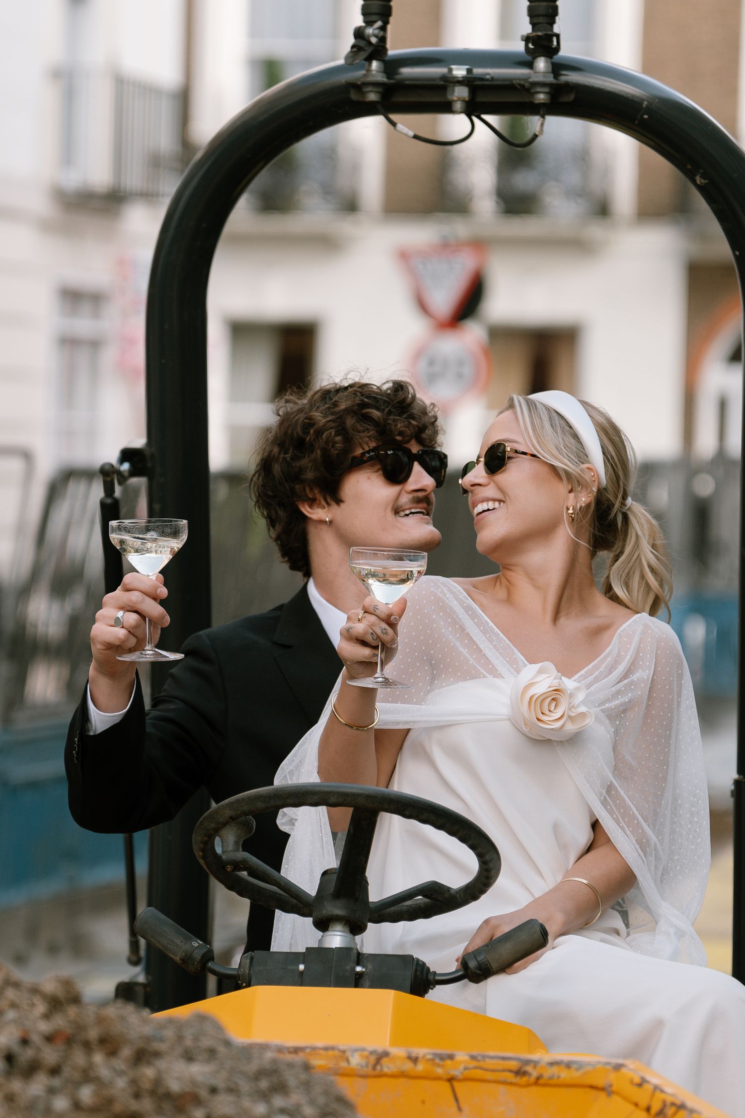 A joyful wedding couple shares a laugh while sitting in a bright yellow construction vehicle.