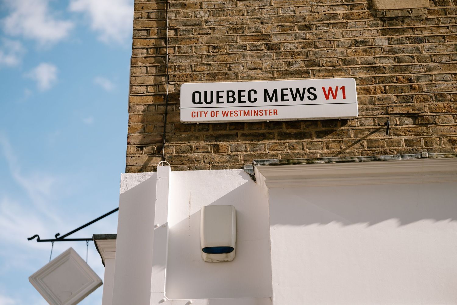 Street sign reading 'Quebec Mews W1' mounted on a brick wall in London.