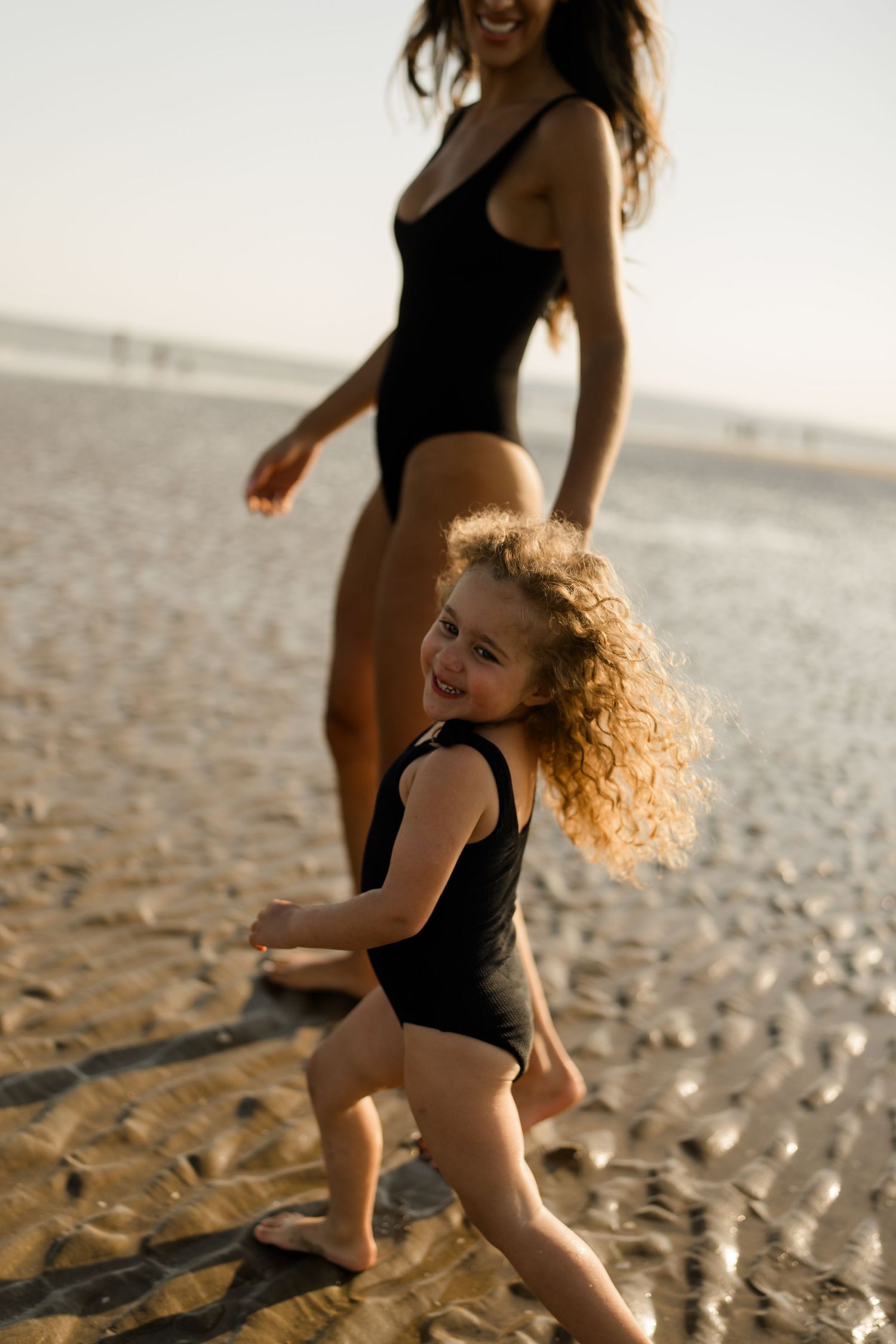 Dancers in black leotards perform dynamic movements on sparkling beach at sunset.