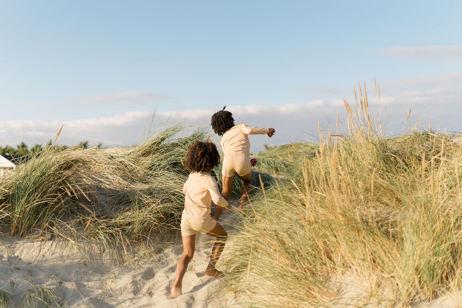 Person climbing up sandy coastal dunes during sunset.