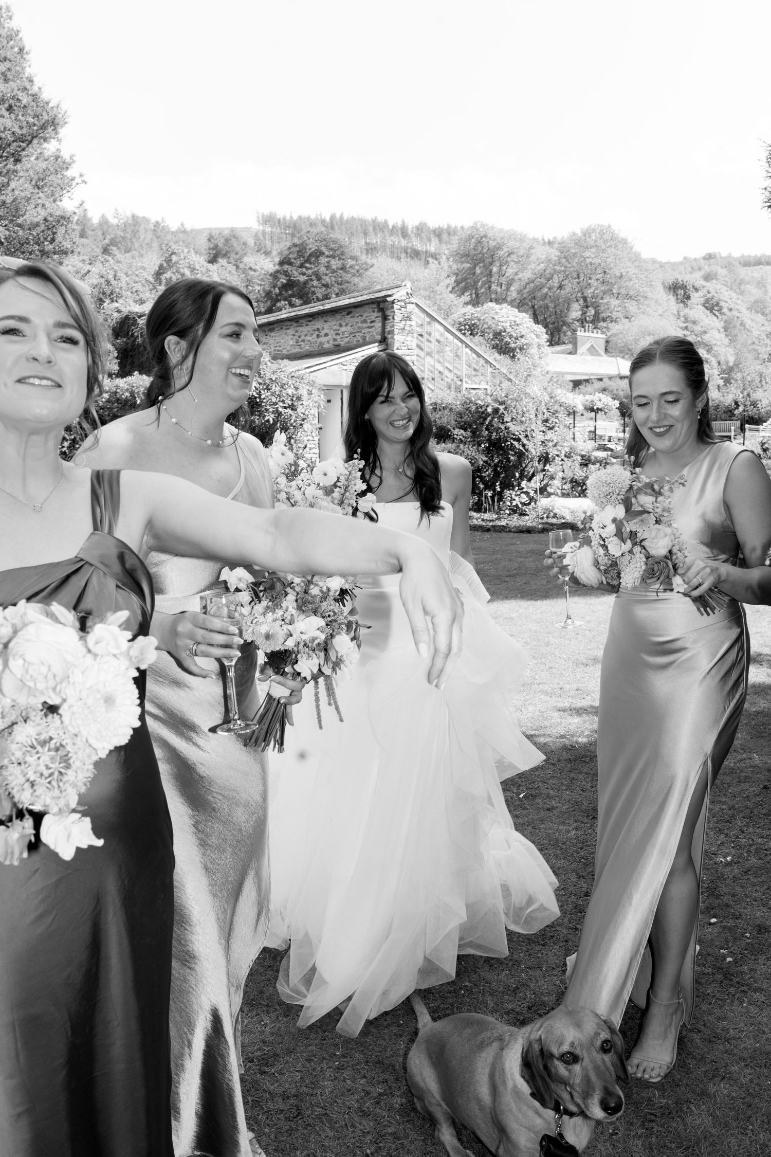 Black and white photo of bridesmaids in formal dresses laughing together outdoors.