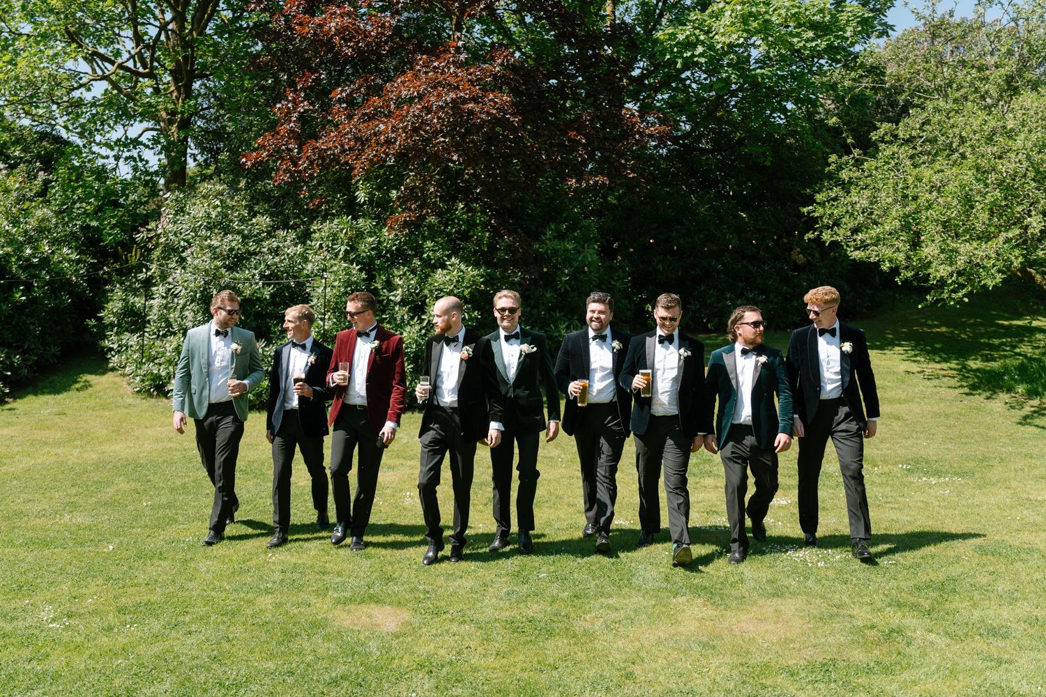 Wide shot of wedding party members lined up on green lawn in formal attire.