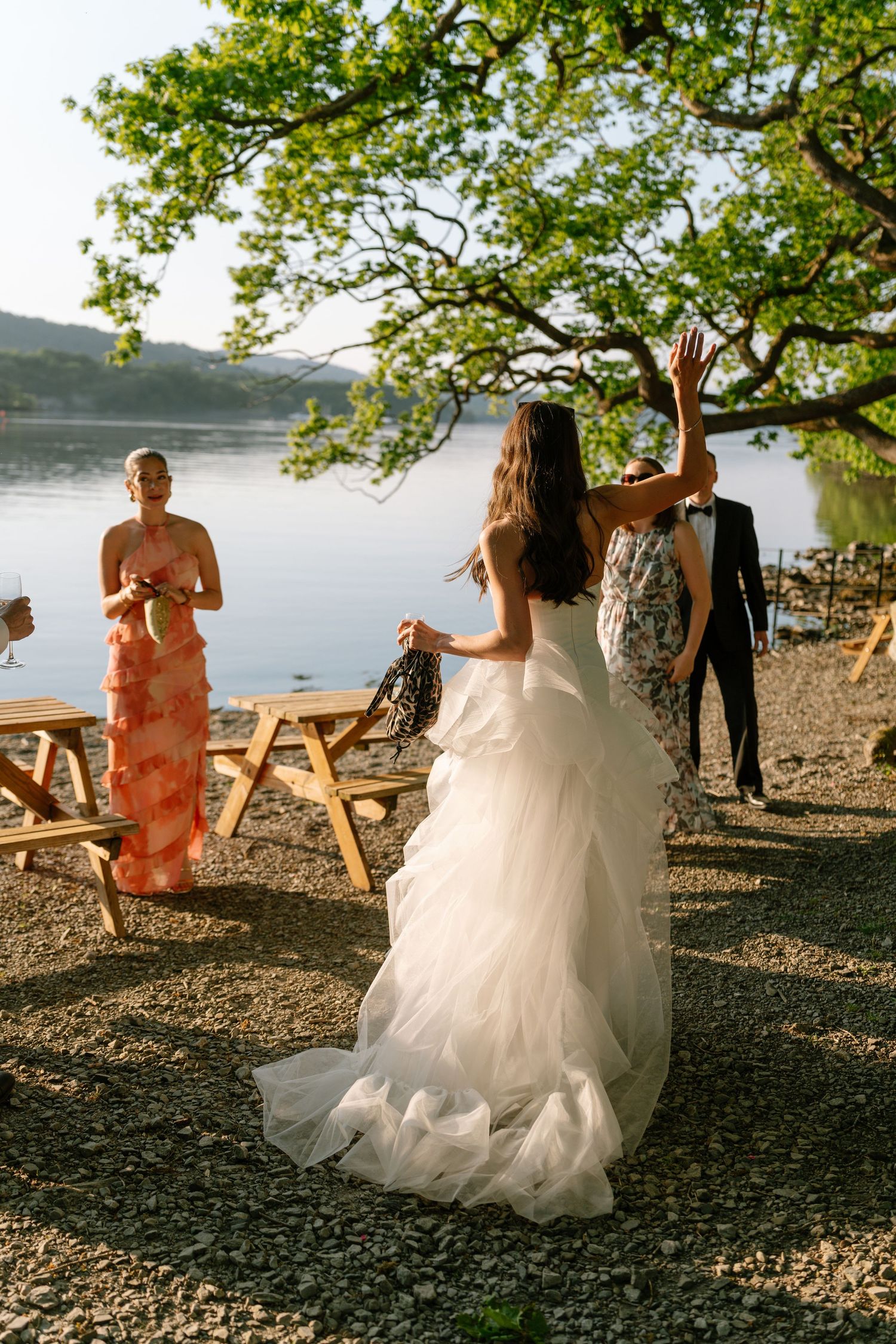 Wedding celebration by a lakeside with guests and a bride in a flowing white dress.