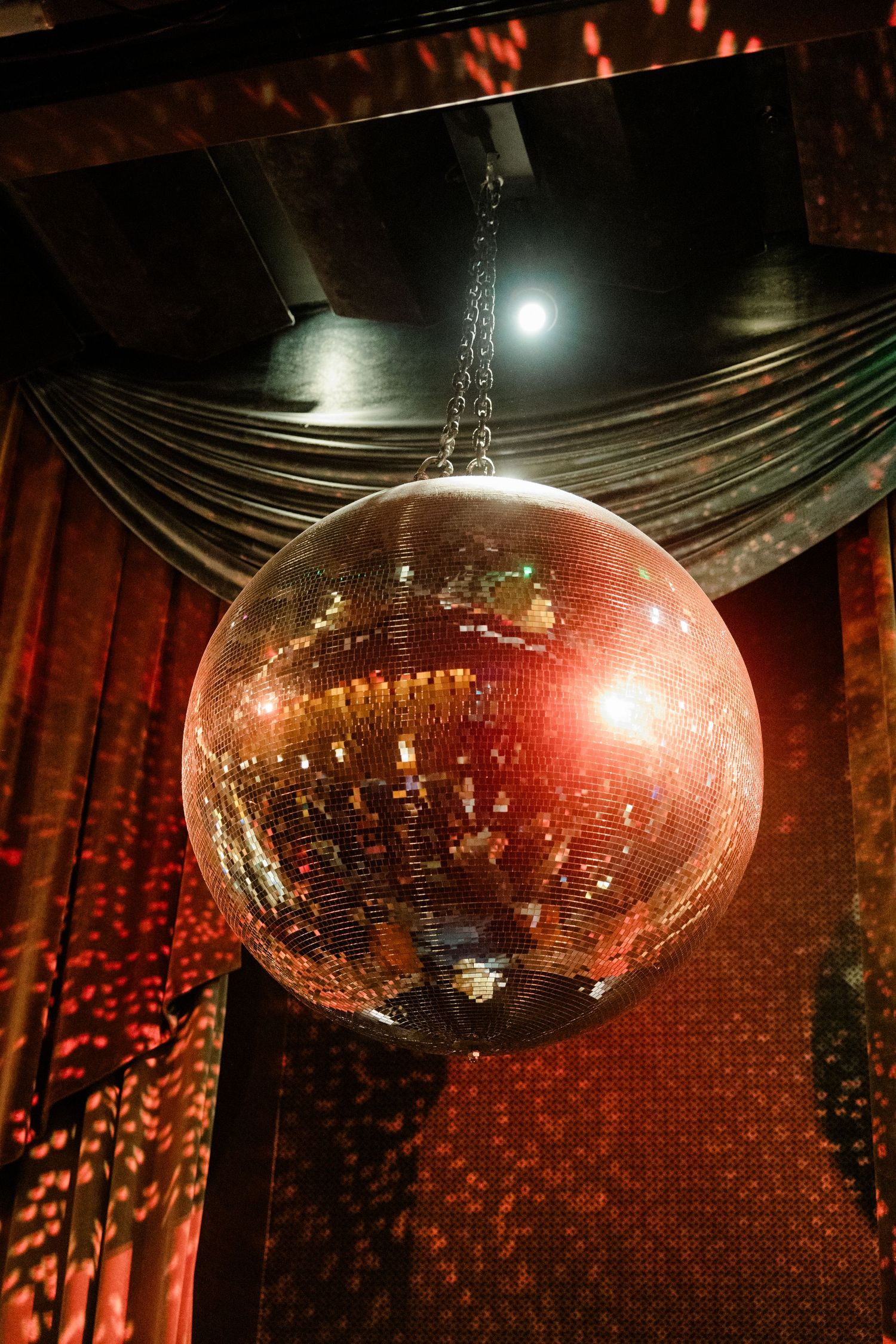 A glowing disco ball hangs dramatically in a dark venue with red ambient lighting.