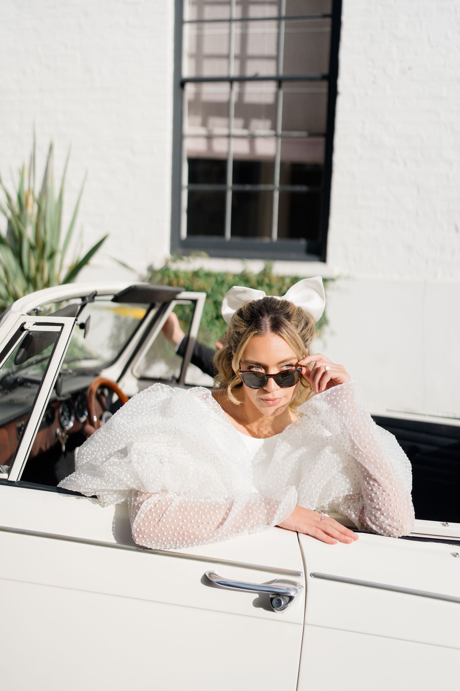 A person in white lace posing in a vintage white convertible car.