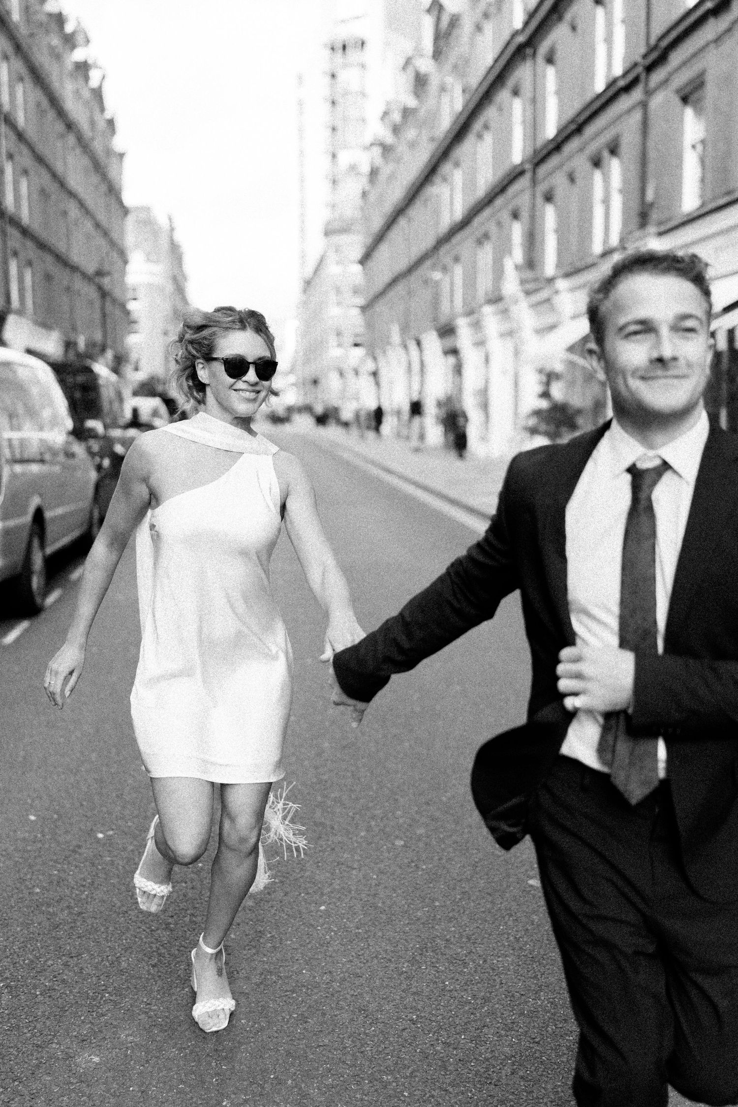 Black and white street photography of couple in formal attire dancing playfully.