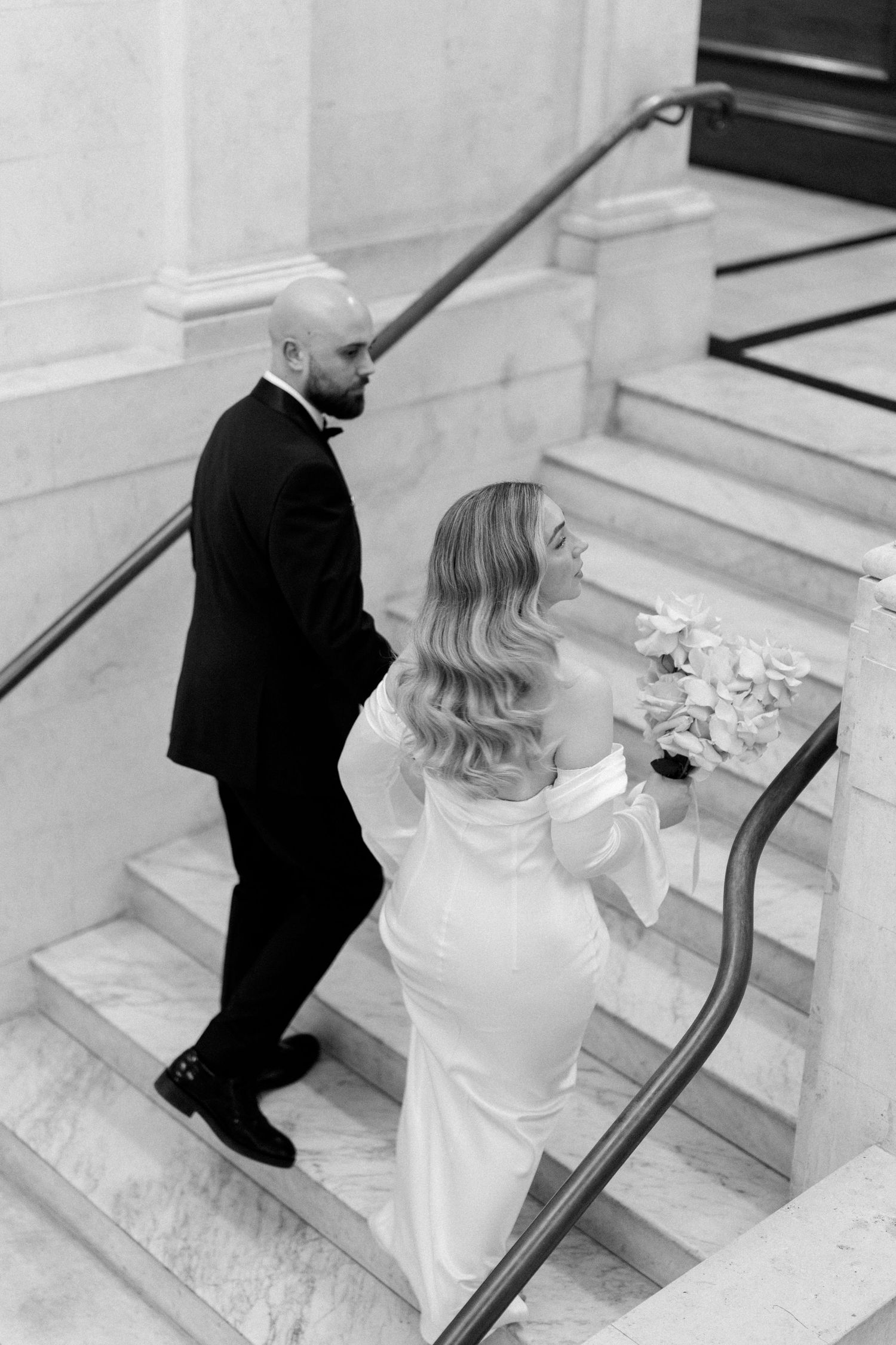 Elegant couple ascending marble stairs at formal venue in black and white photography.