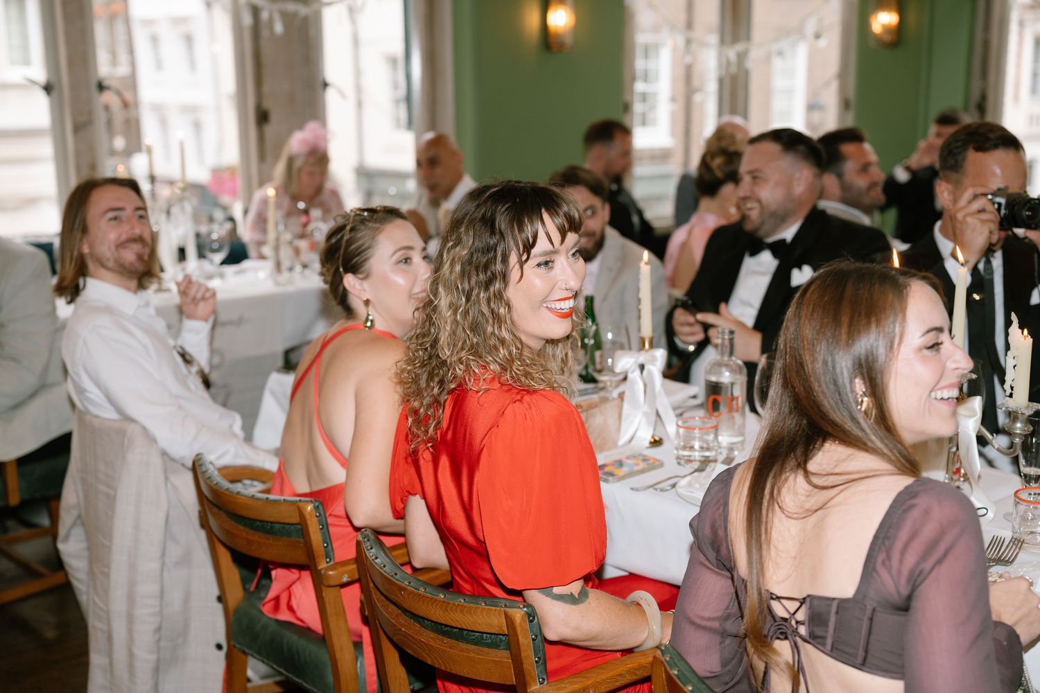 Wedding reception guests enjoying themselves at decorated tables with natural lighting.
