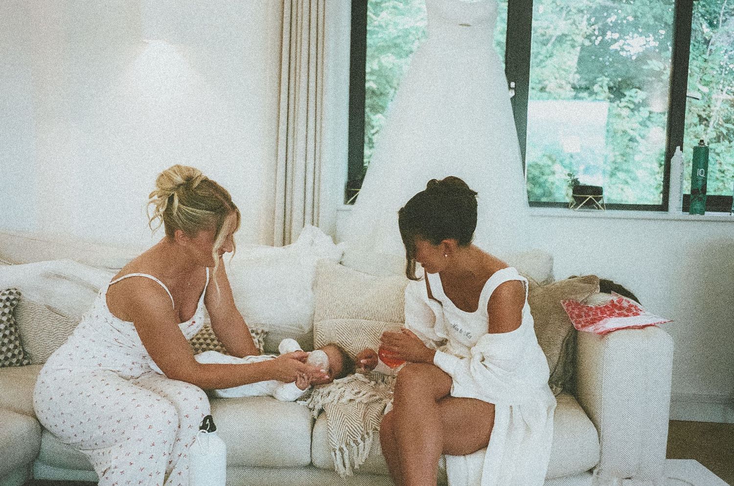 Two people in white dresses sit on a couch preparing for a wedding ceremony.