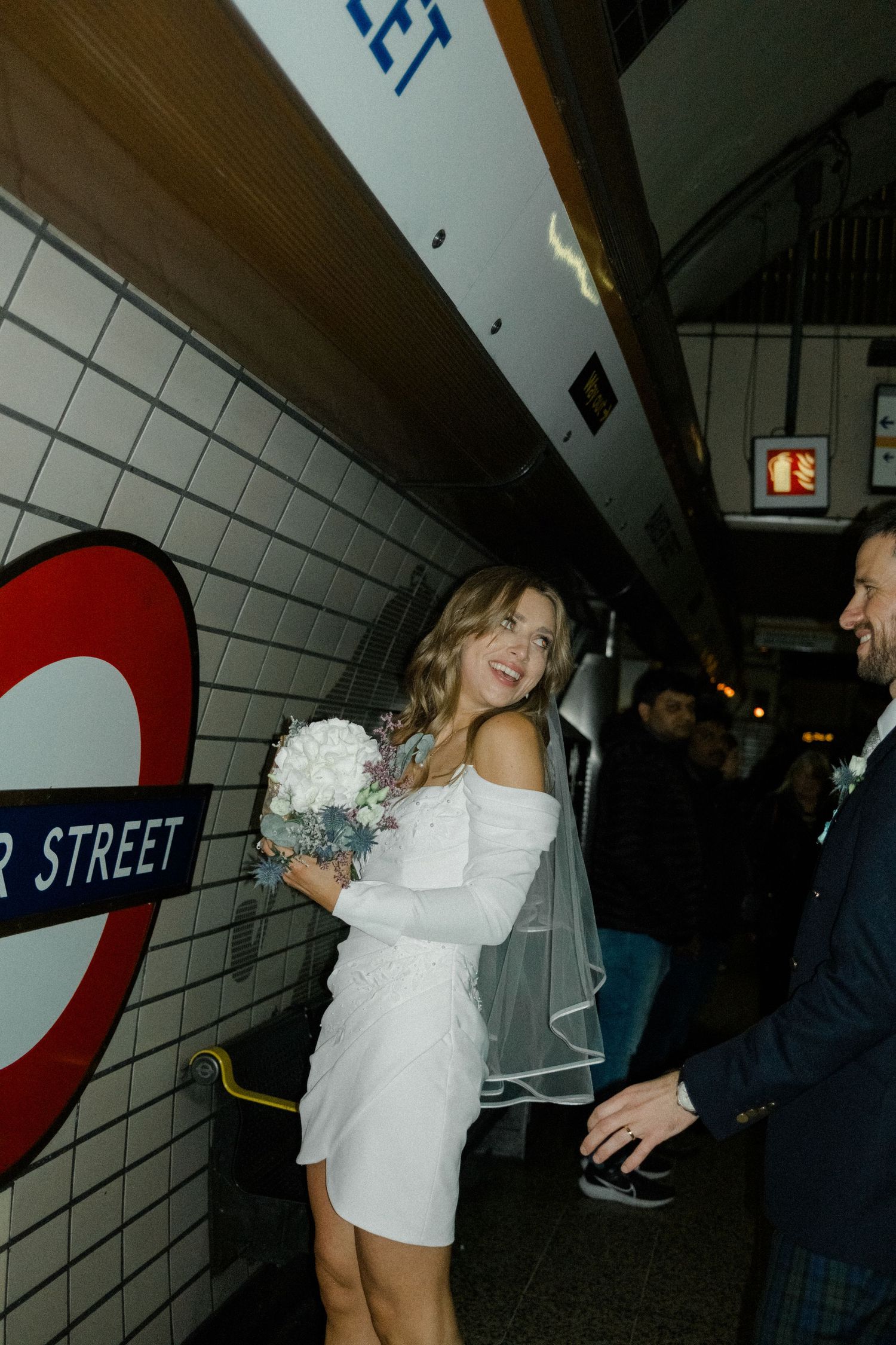 People celebrating and dancing in a London Underground station with iconic white tiled walls and roundel signage.