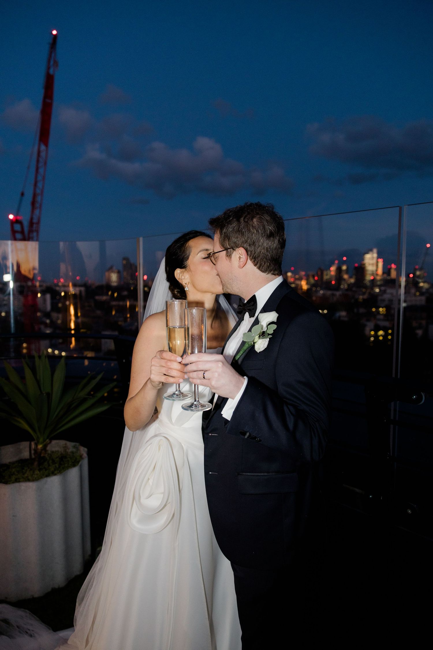 Wedding couple shares romantic moment on rooftop against city night skyline.