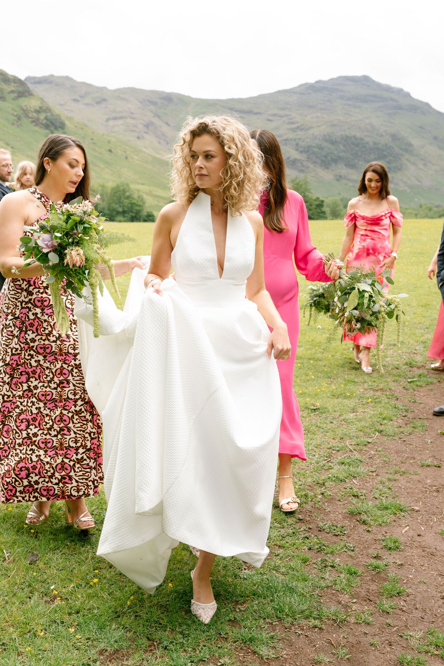 Bridal party walking and holding their dresses on mountain trail.