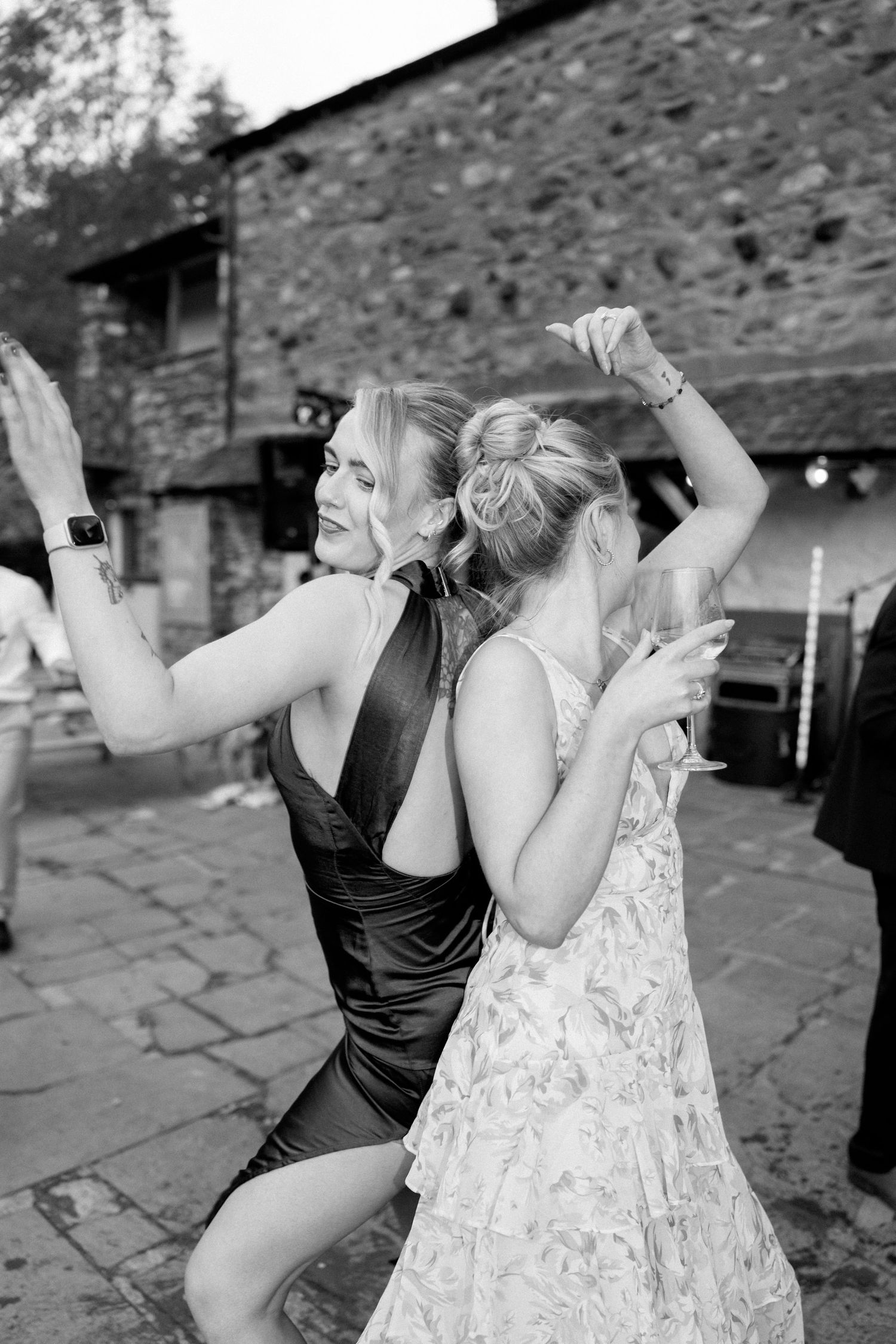 Wedding guests dancing joyfully outside a stone building.