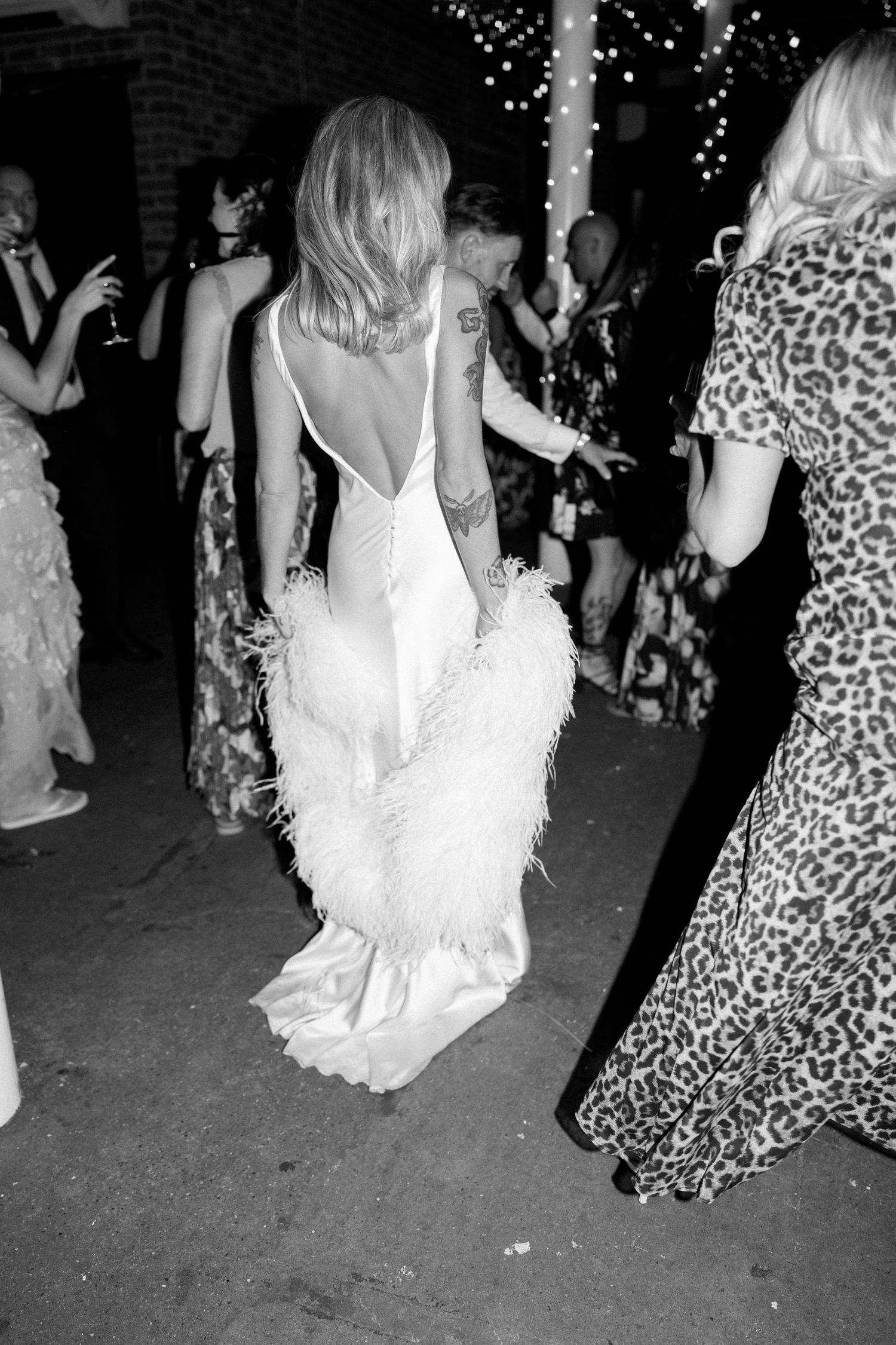 Wedding celebration with guests dancing in elegant dresses under twinkling lights.