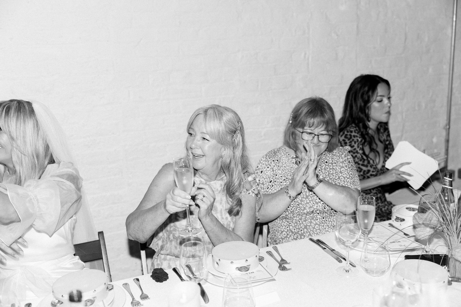 Black and white photo captures candid moments of guests dining at a wedding reception.