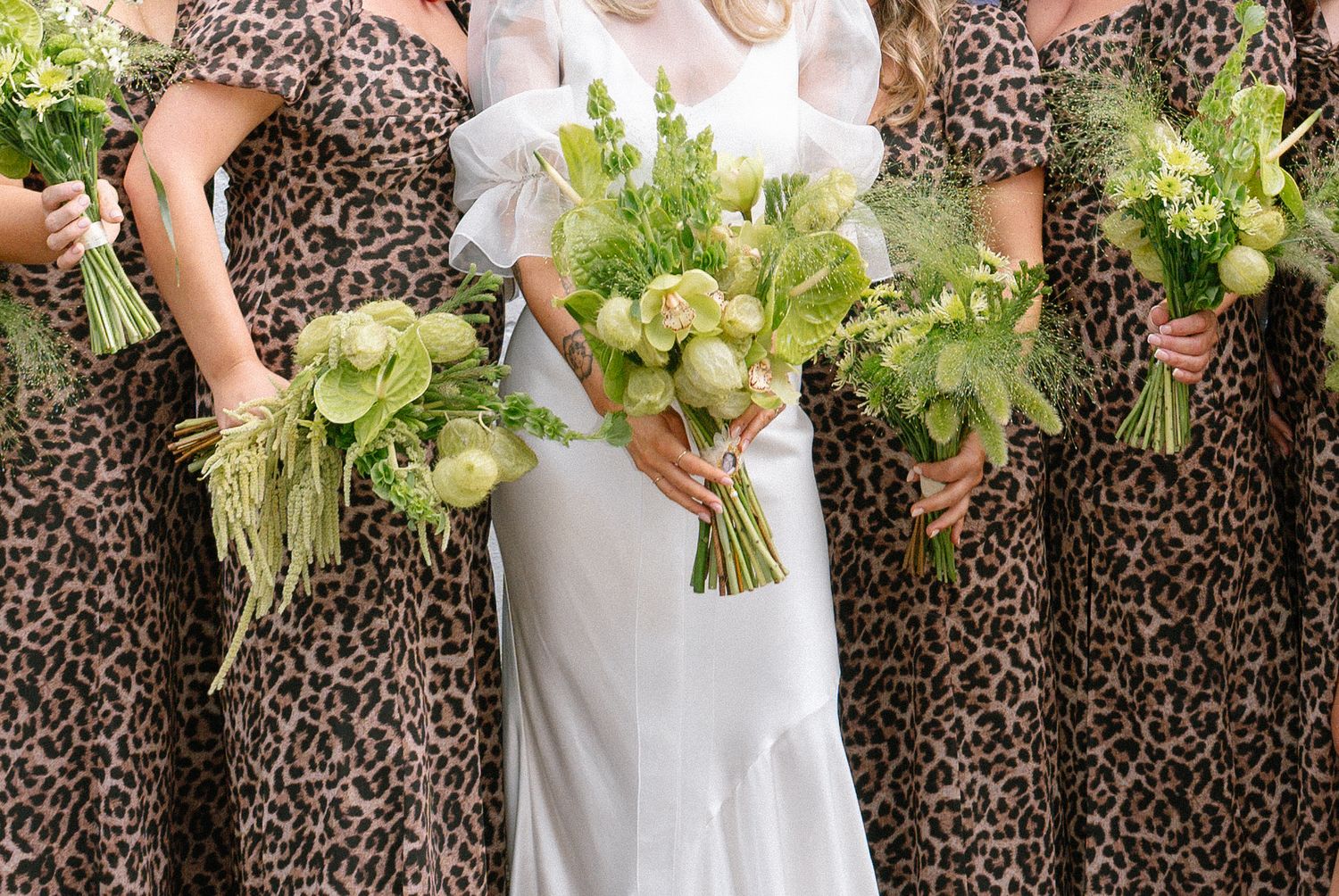 Bride in white dress with bridesmaids in leopard print dresses holding green bouquets.