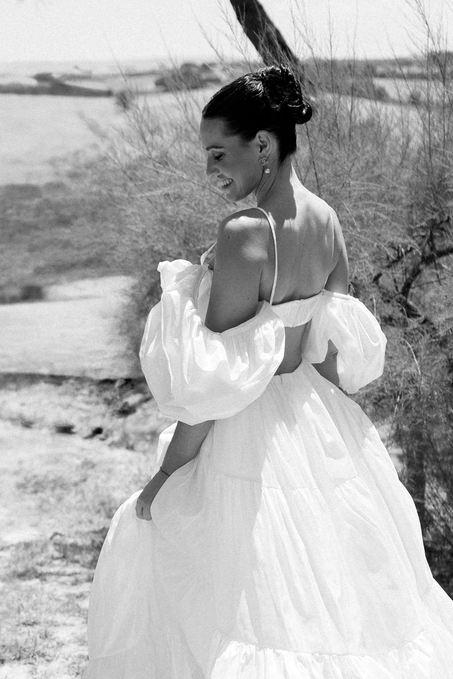 Flowing white wedding dress captured in motion against rustic landscape in black and white.