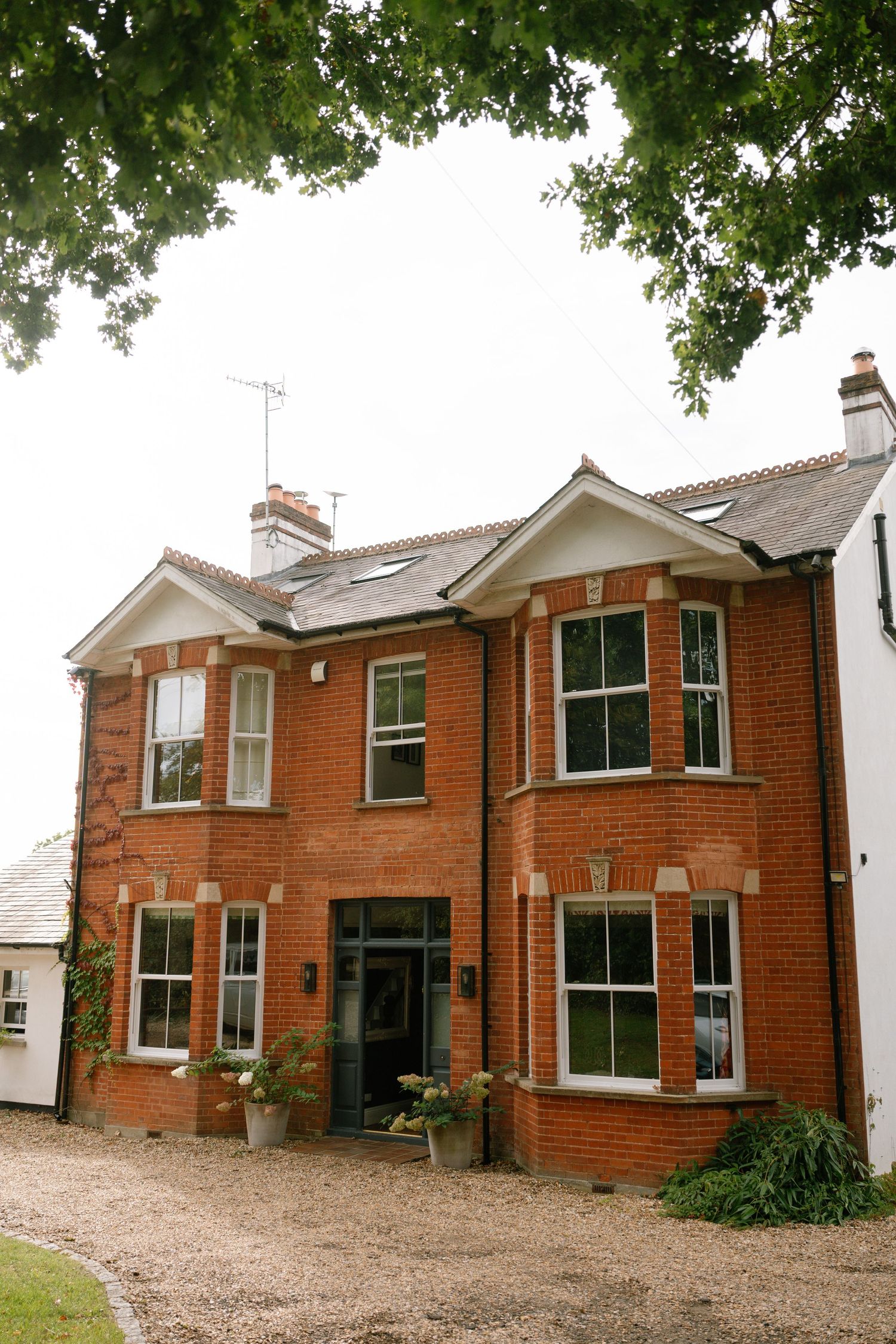 Row of traditional red brick houses with white trim and gravel driveways under leafy trees.