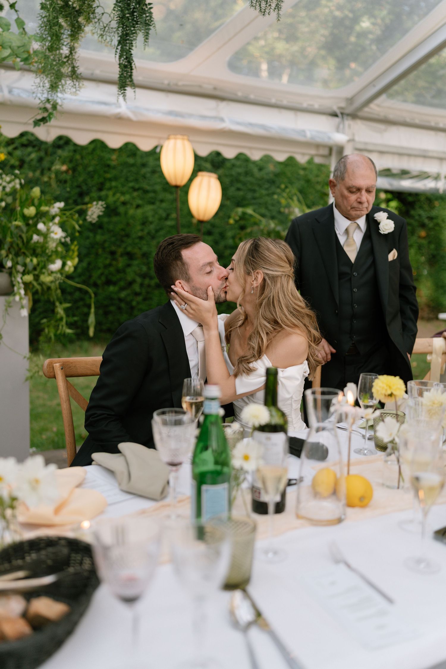 Tender moment captured during wedding reception under tent with glowing lanterns.