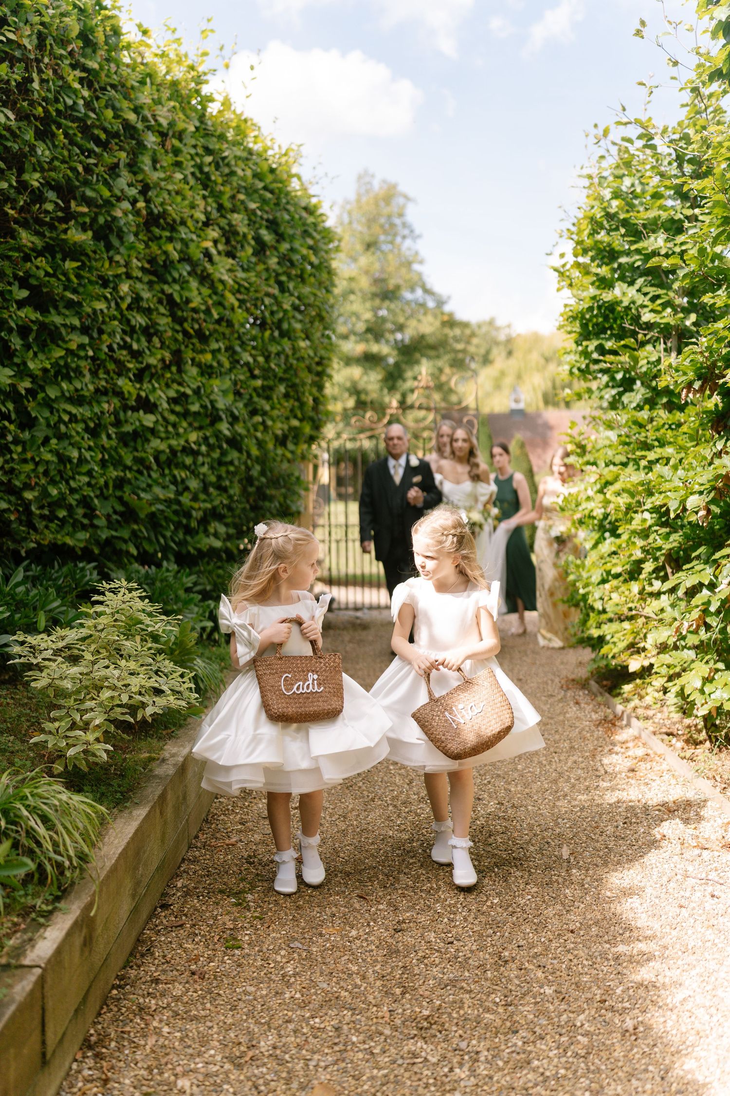 Young attendants walking garden path carrying personalized wicker baskets.