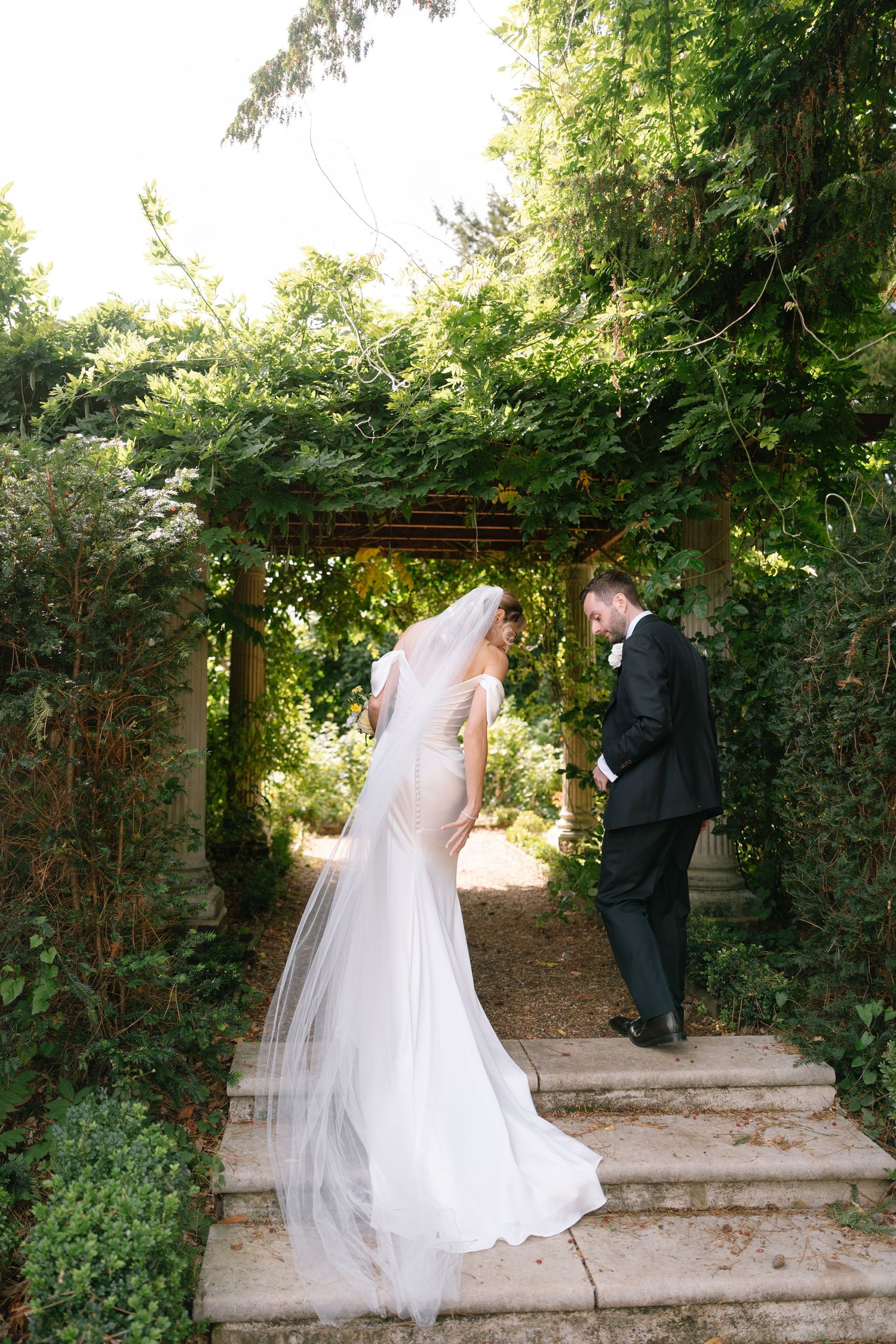 Couple walking along garden pathway with ivy covered walls during wedding photoshoot.
