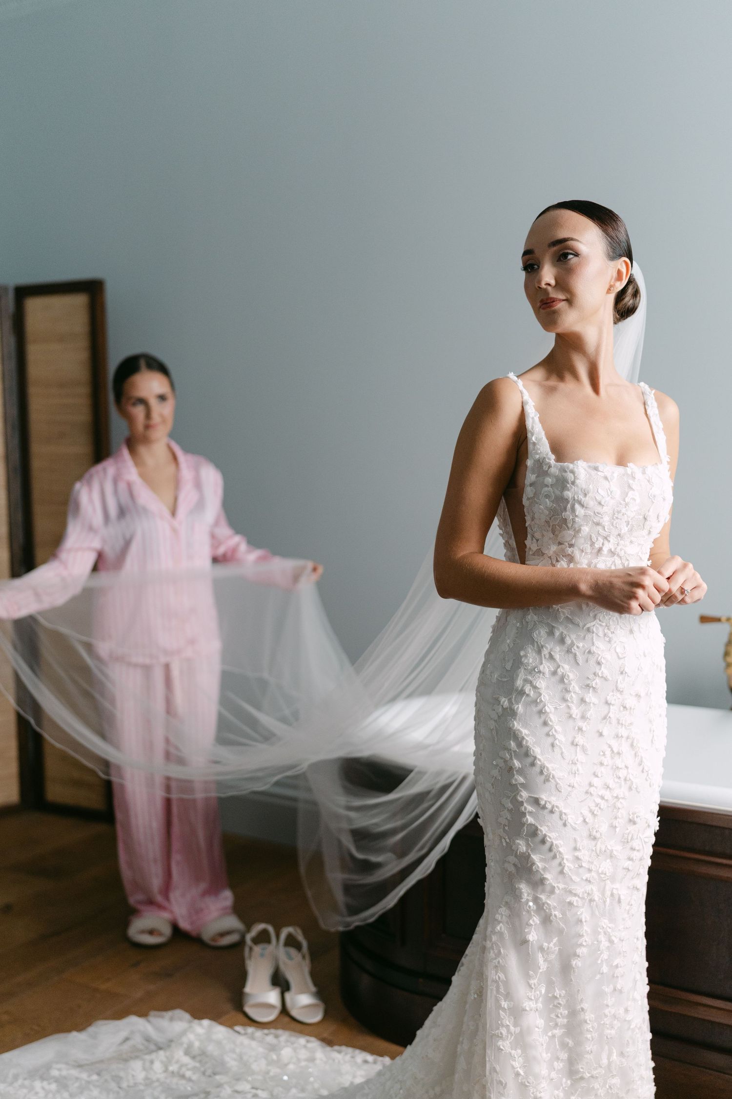 Bride getting ready in a fitted white wedding gown with flowing tulle veil.