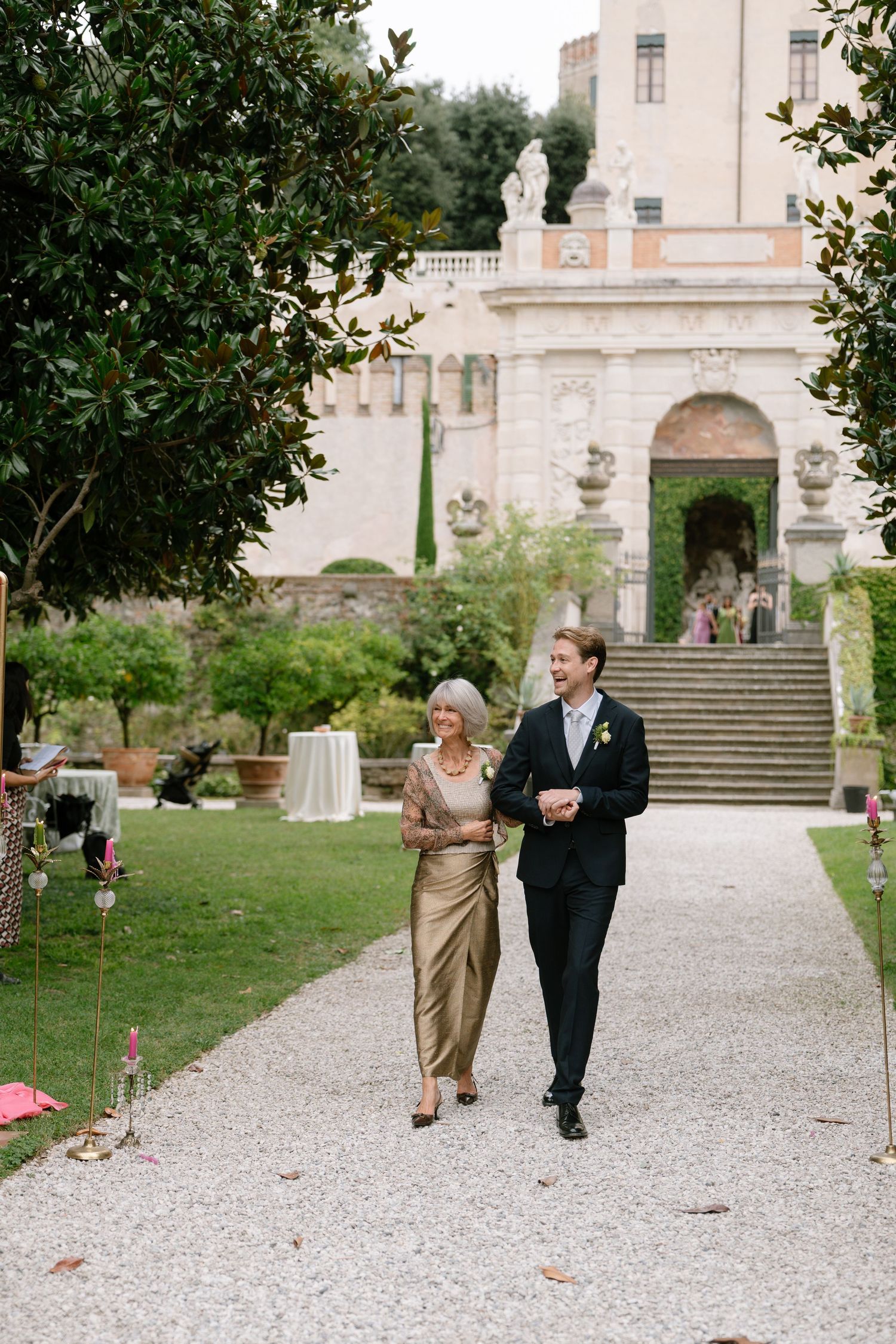 Formal event guests walking along a path in front of an elegant villa.