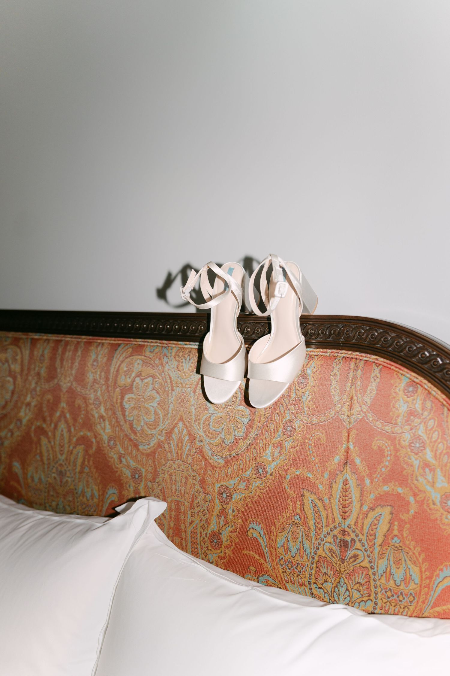 Elegant white bridal shoes resting on a vintage peach and gold damask headboard.