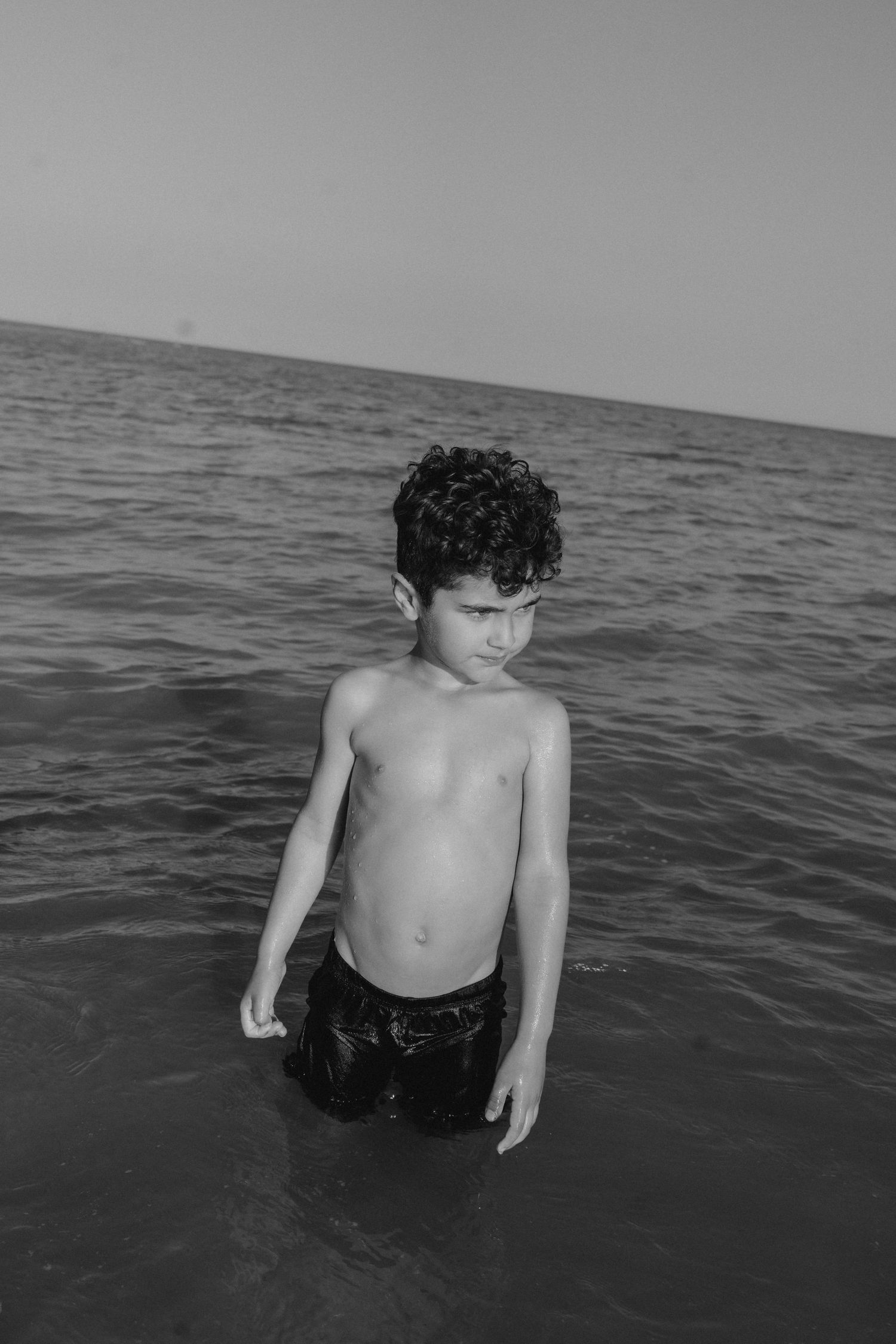 A child wades through dark ocean waters in black and white photography.