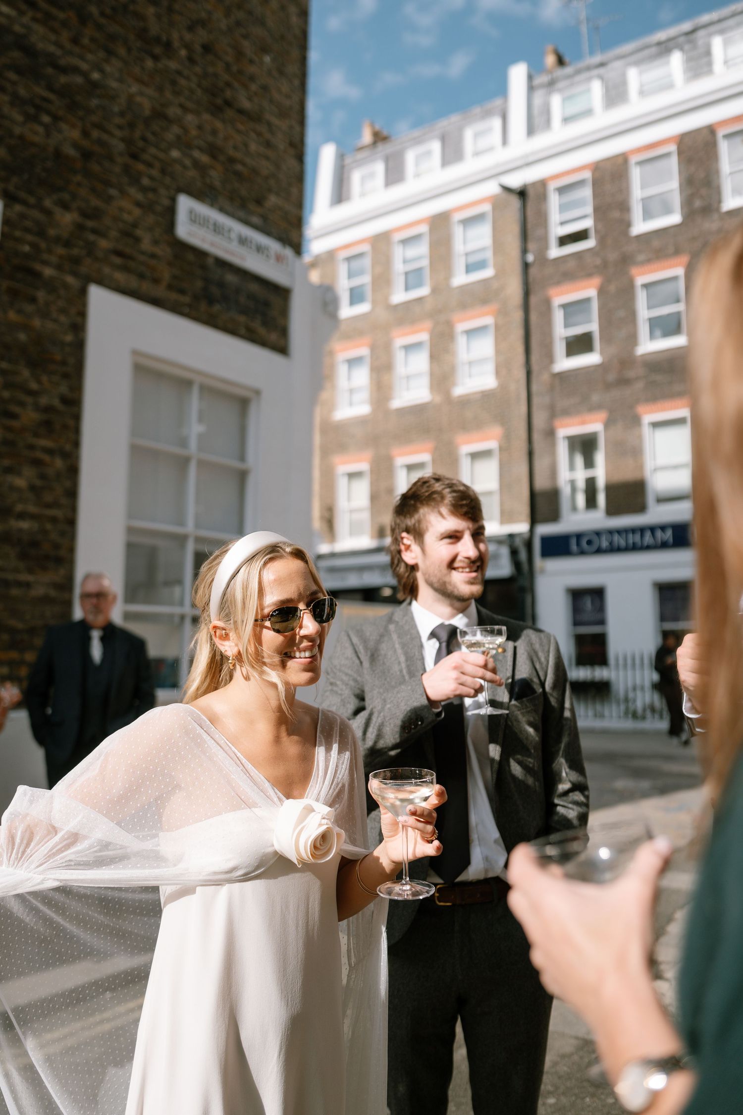 Wedding guests toasting with champagne glasses outside a historic brick building.