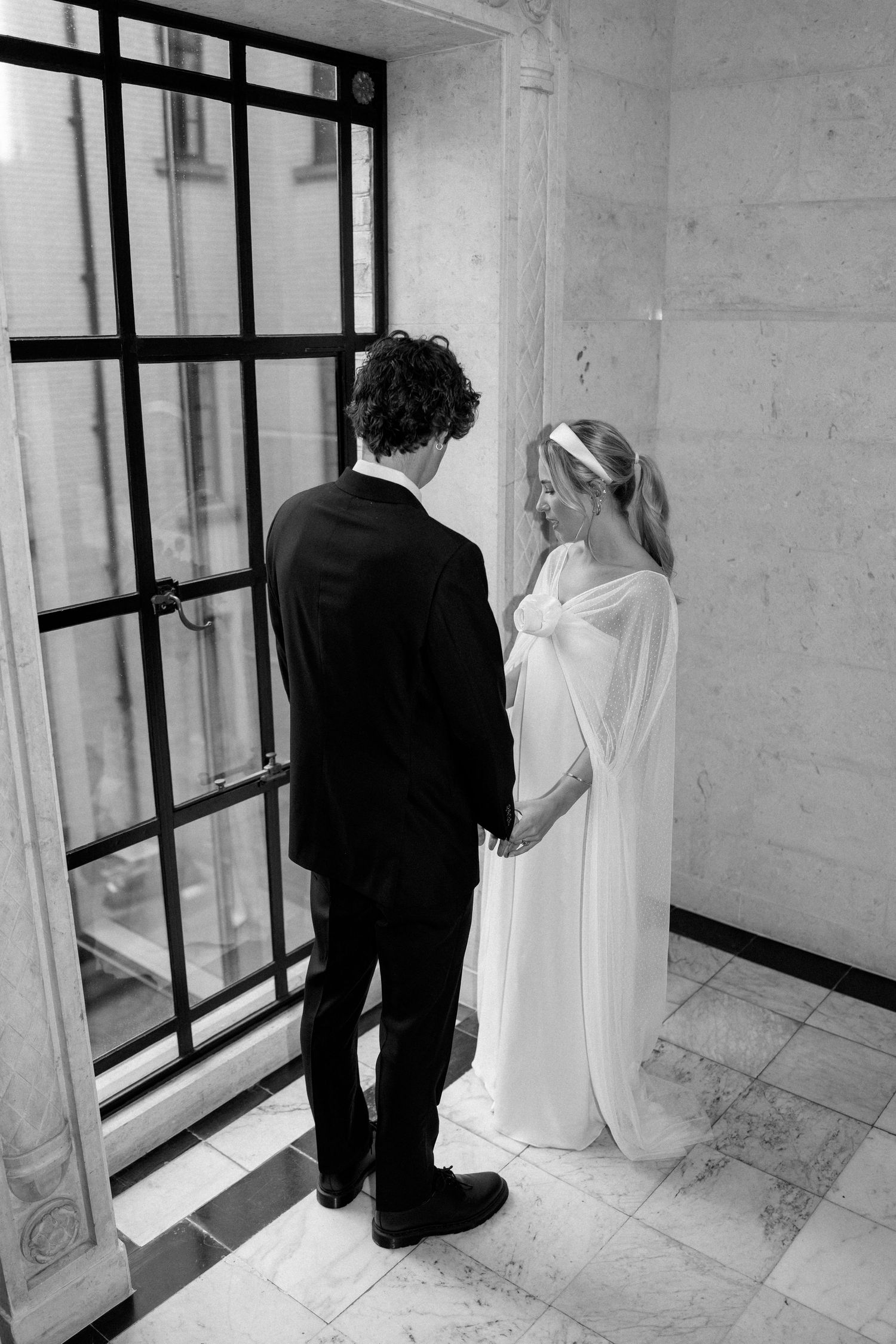 Black and white sequence showing newlyweds walking together near large windows in an elegant building.
