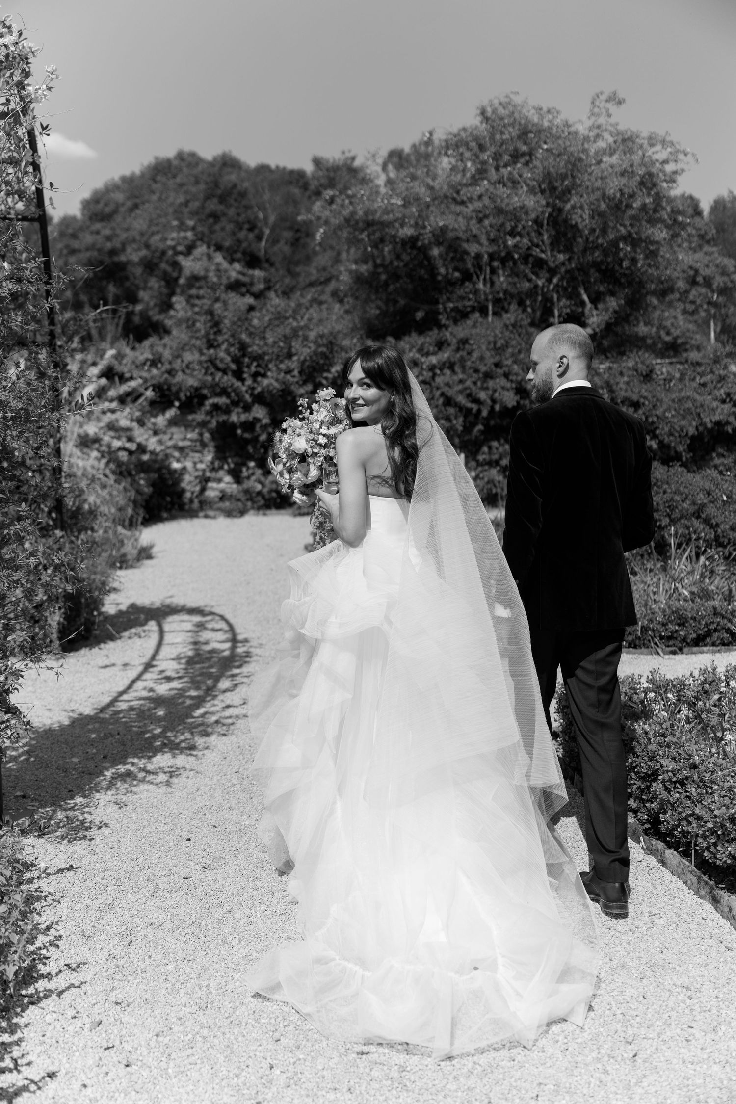 Black and white capture of wedding procession on a winding garden path.
