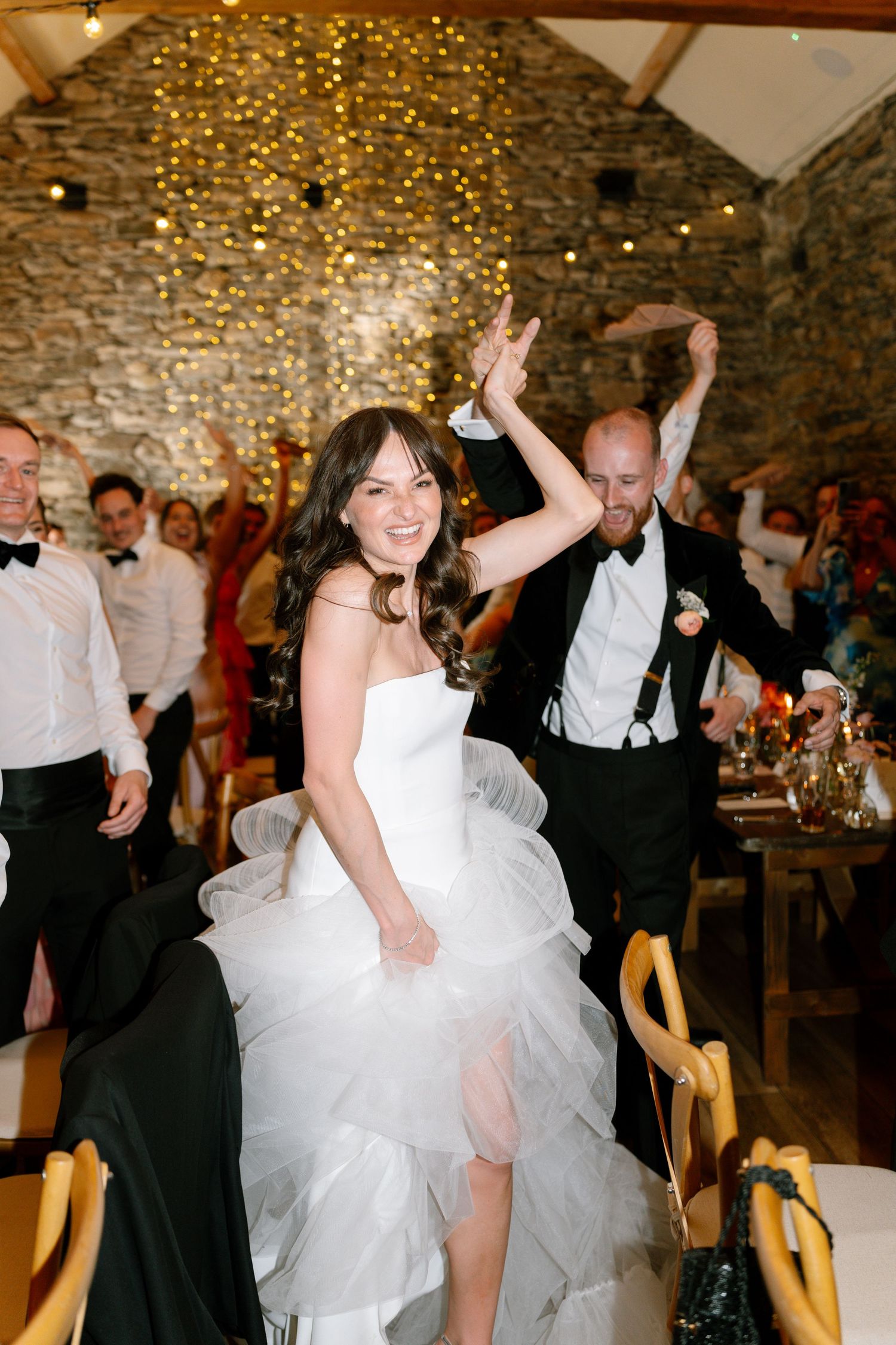 Energetic dancing at wedding reception under warm string lights.