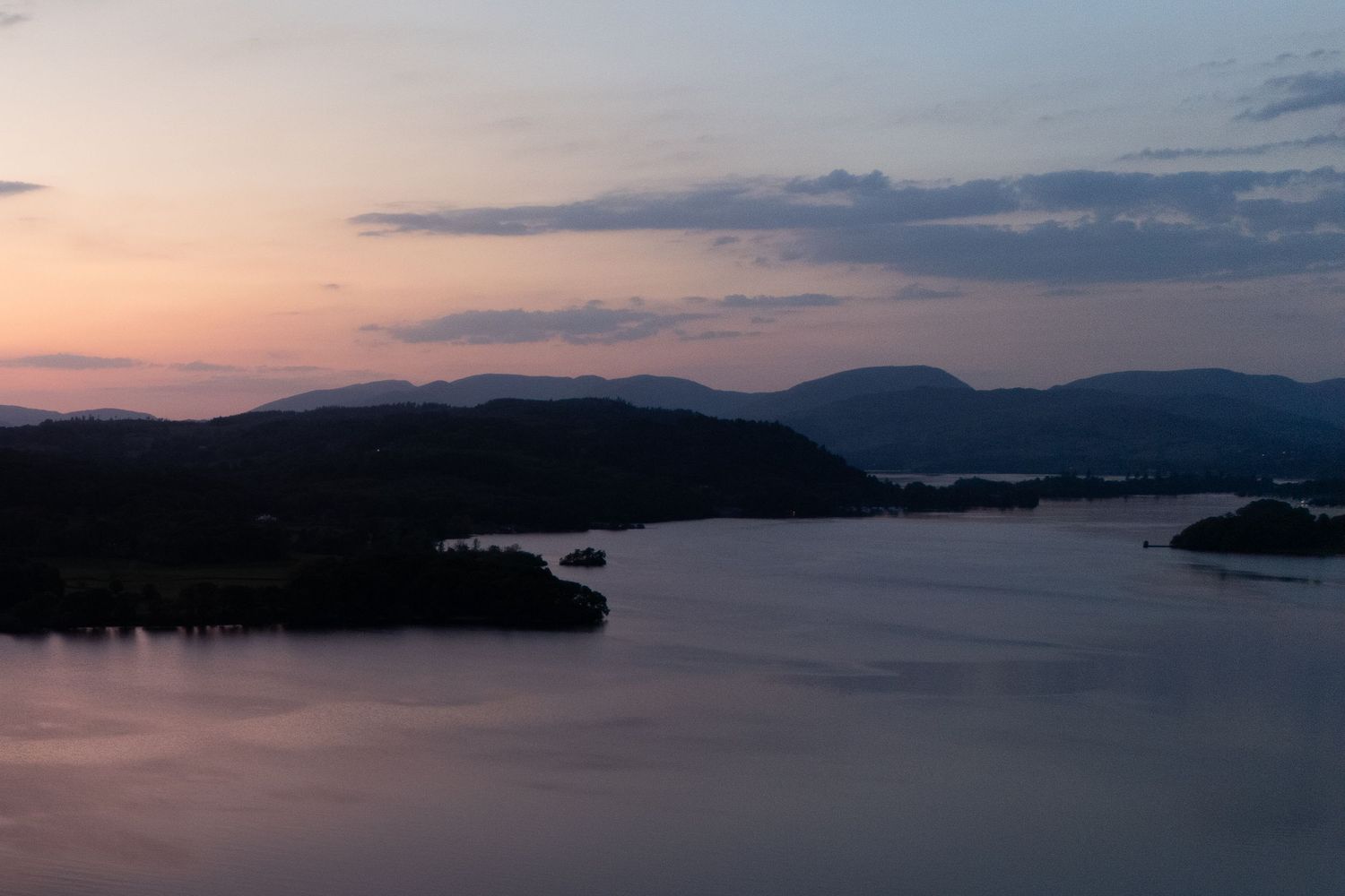 Sunset panorama over a peaceful lake with mountains and islands in the distance.