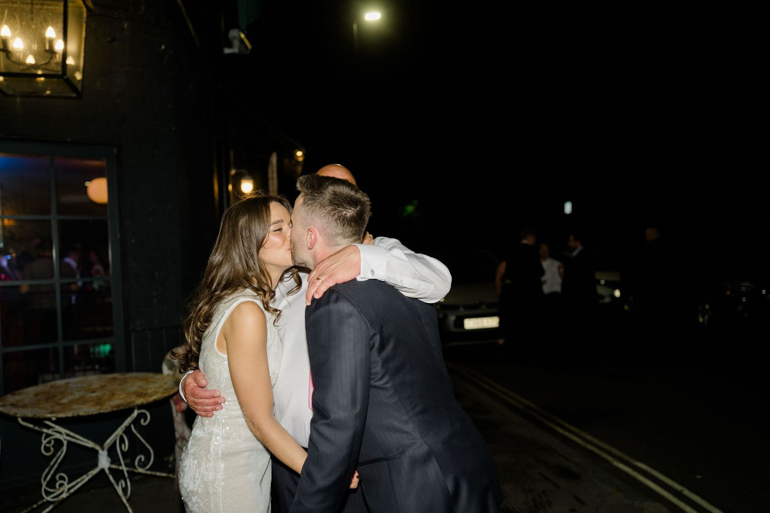 Bride and groom share a tender kiss outside at night following their wedding celebration.