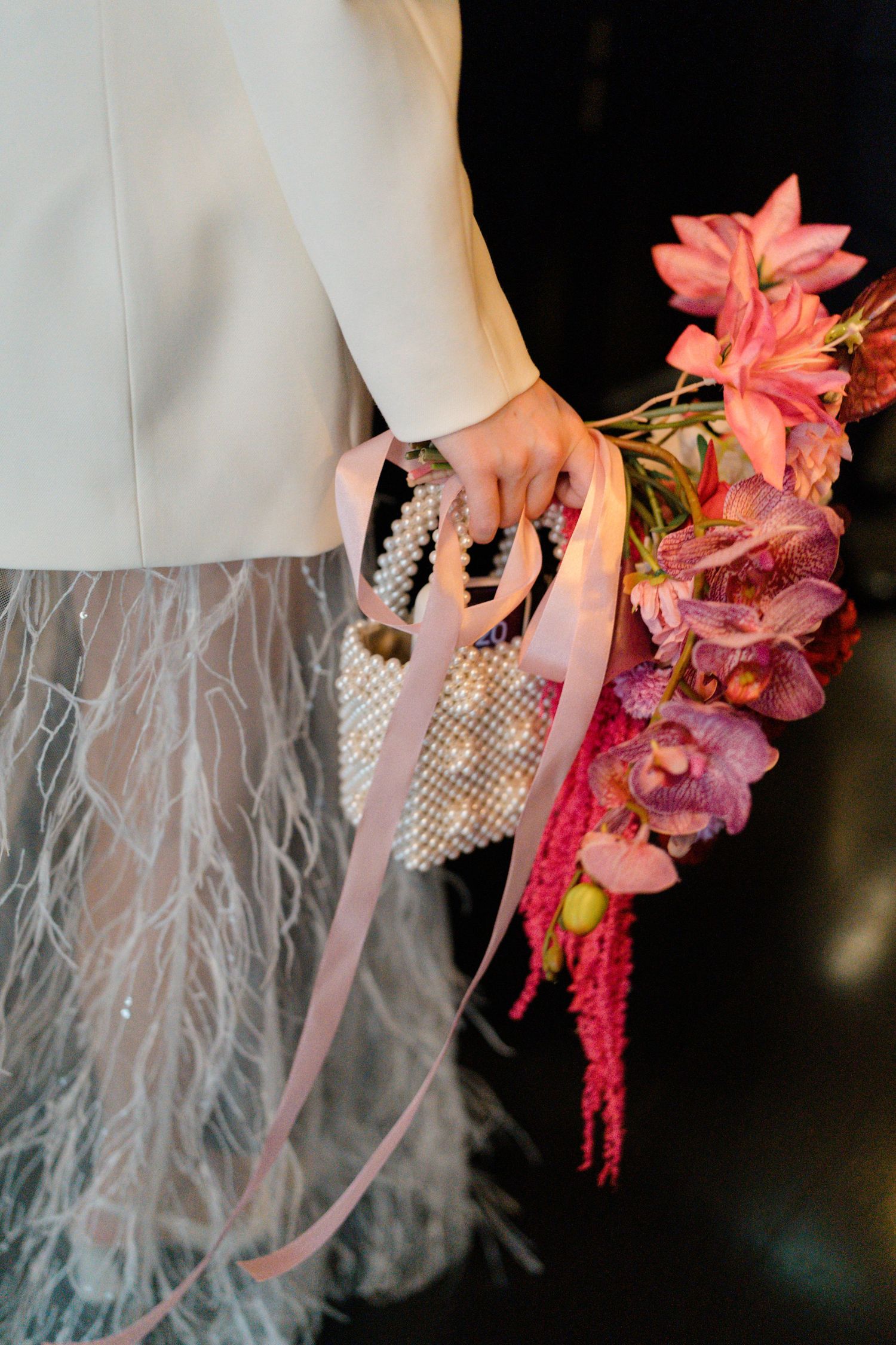 Bride holding pink floral bouquet and pearl beaded bag with feather skirt detail.