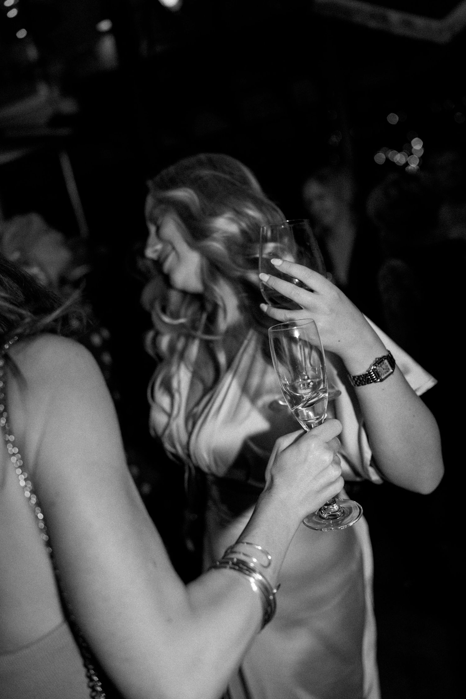 Wedding guest in evening wear laughs while holding champagne flute at lively reception celebration.