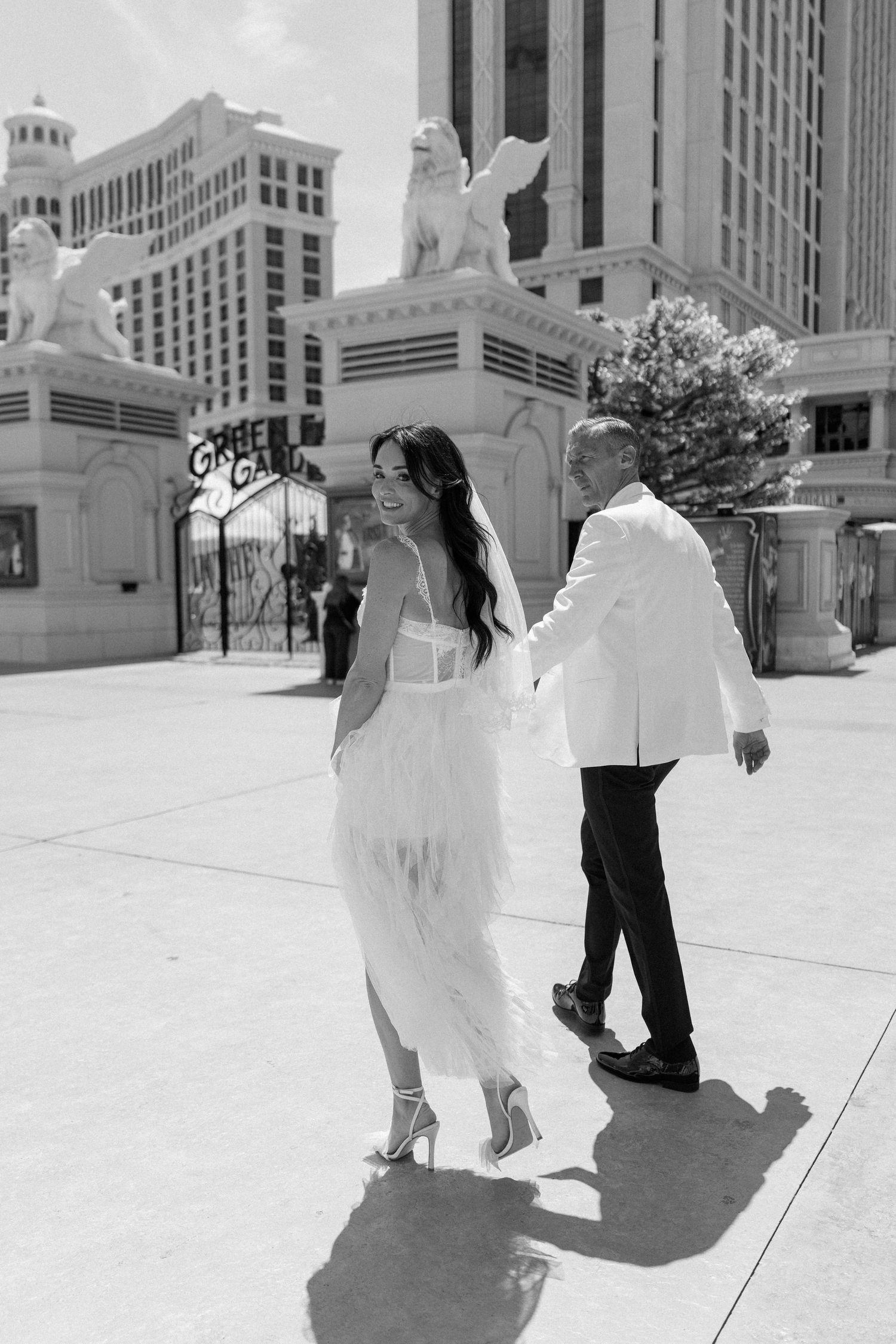 A black and white photo of a couple walking past decorative statues at a Las Vegas hotel.