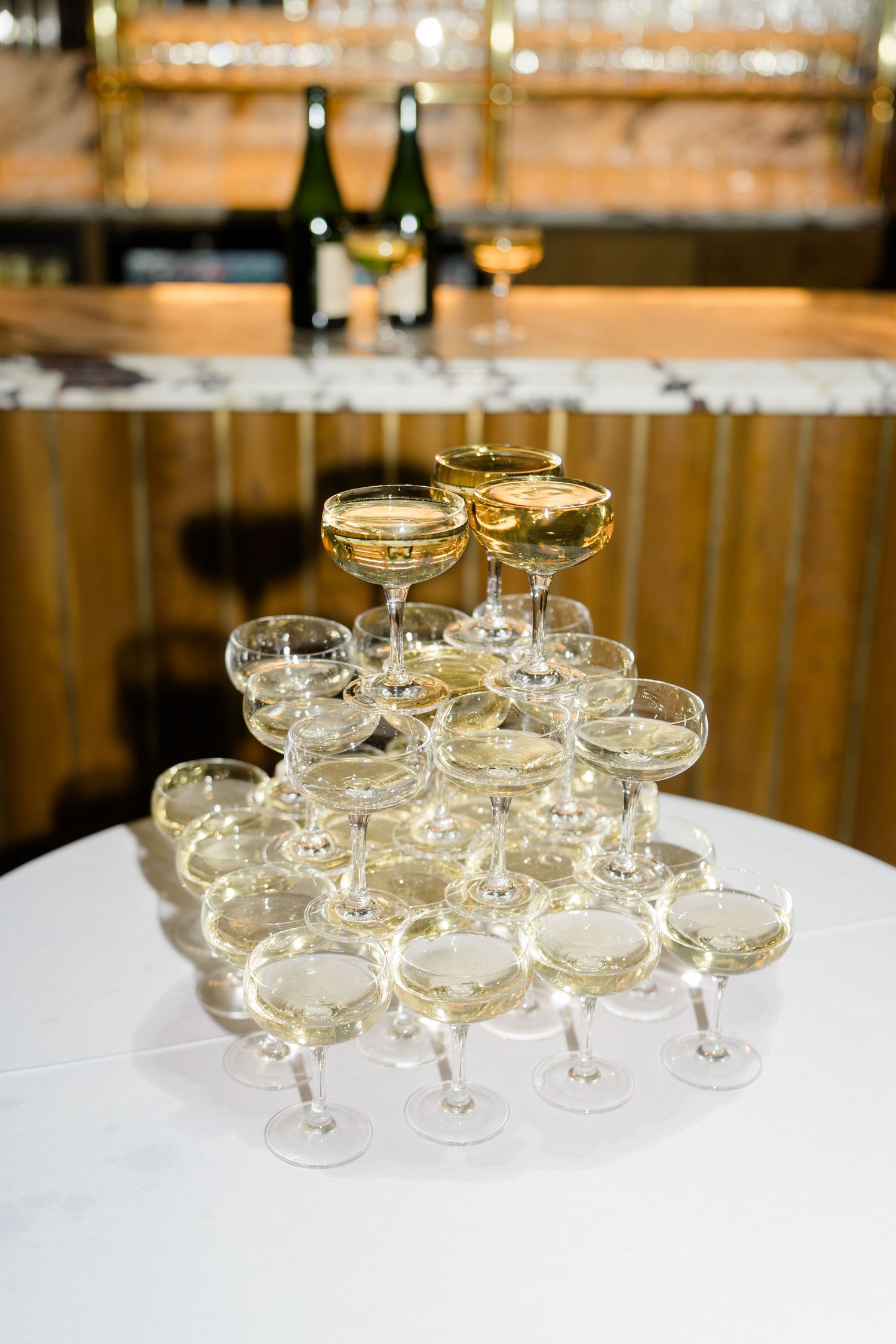 Pyramid tower of champagne coupe glasses filled with sparkling wine on white tablecloth at wedding reception.