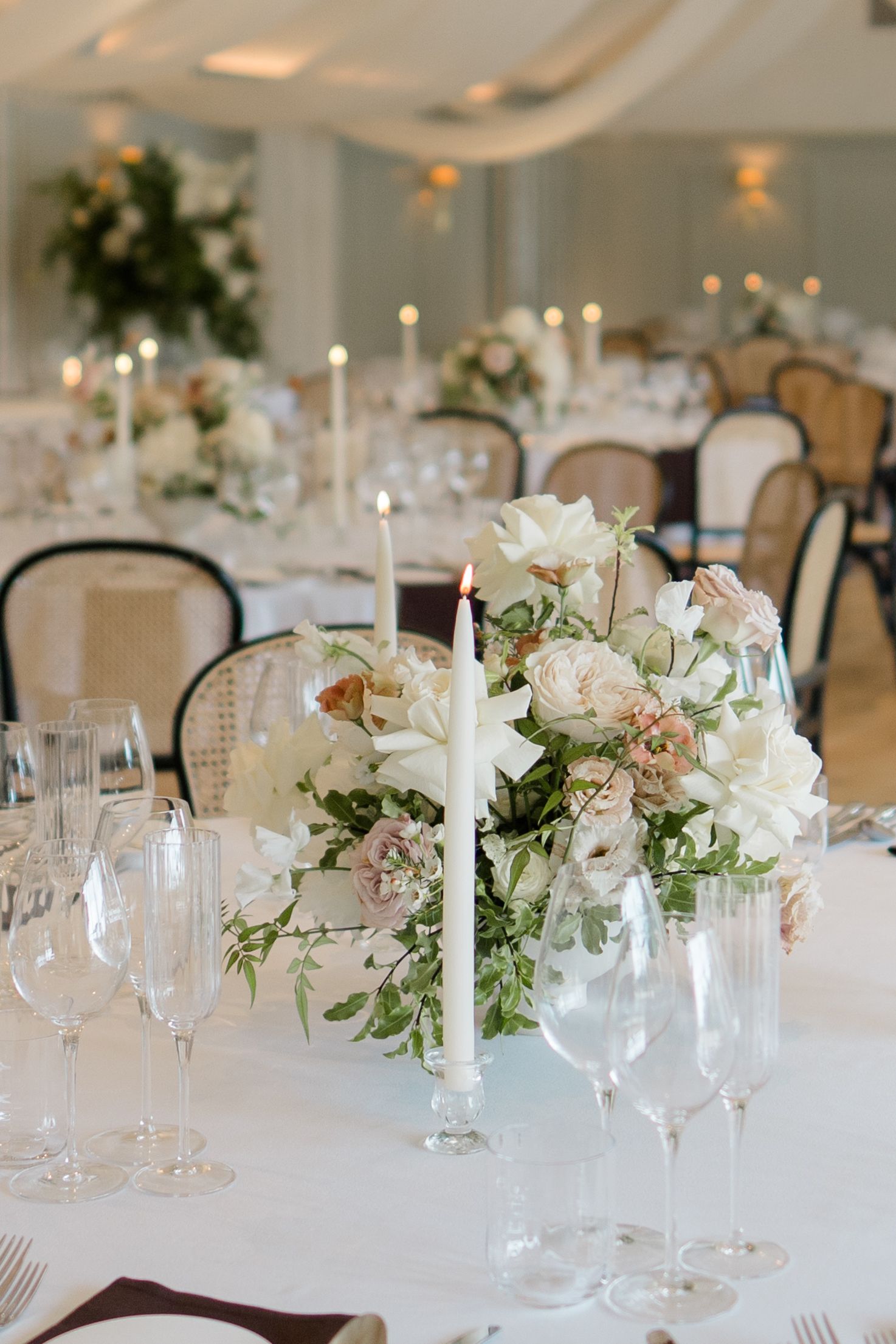 Elegant wedding reception table with white floral centerpiece, lit taper candle, and crystal glassware.